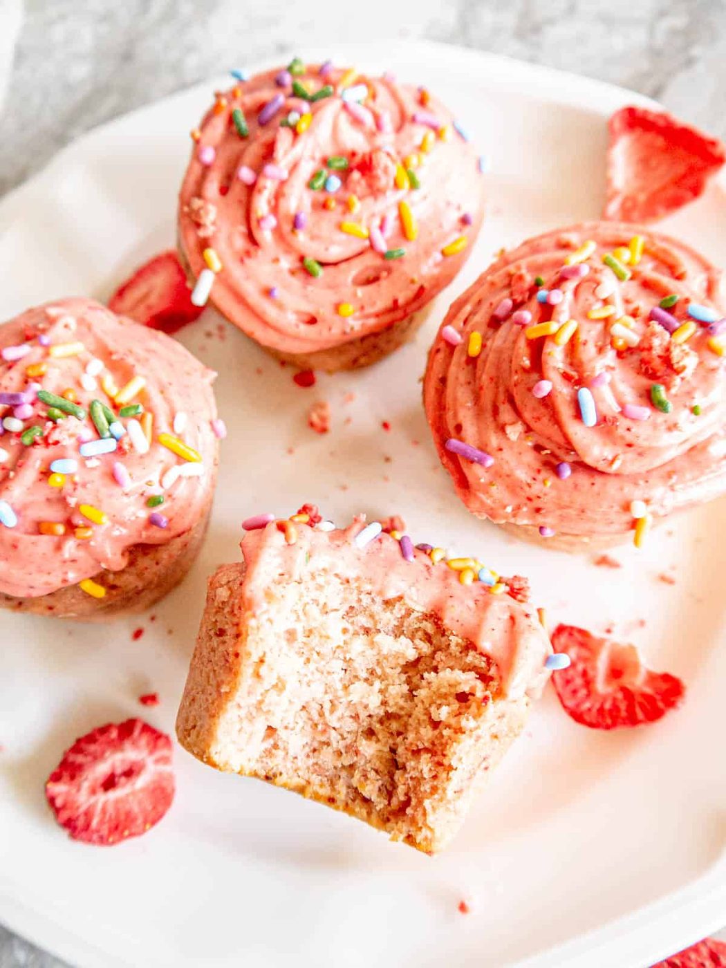 A bite taken out of a strawberry cupcake.