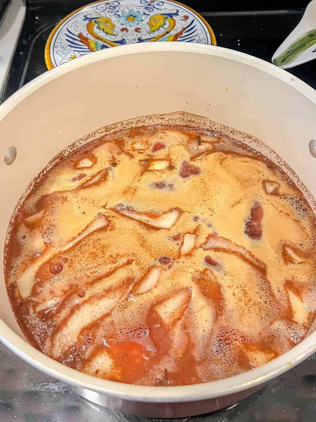 Poached pears in red wine and orange juice cooking on the oven.