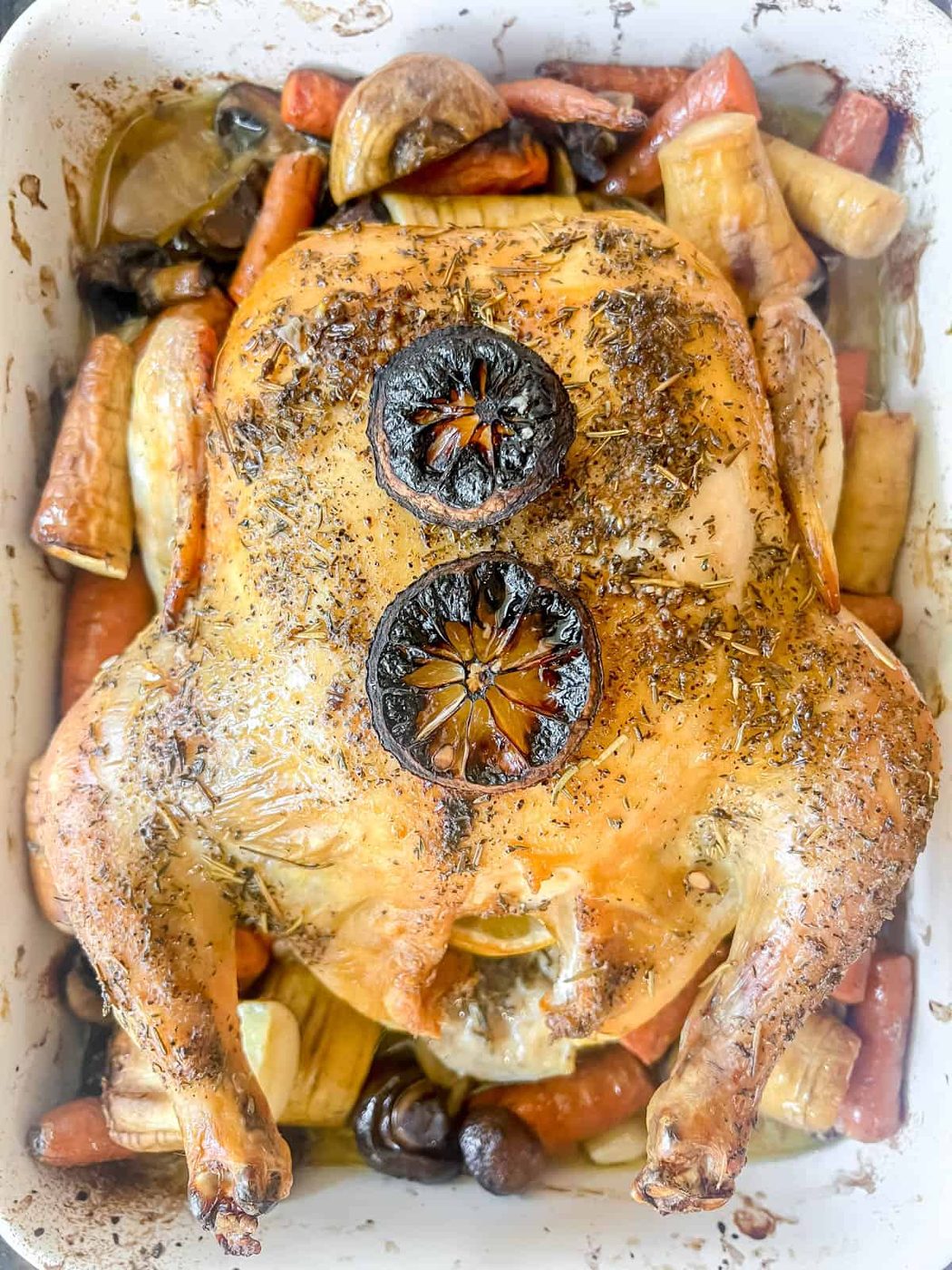 Roast chicken just pulled out of the oven surrounded by root vegetables.