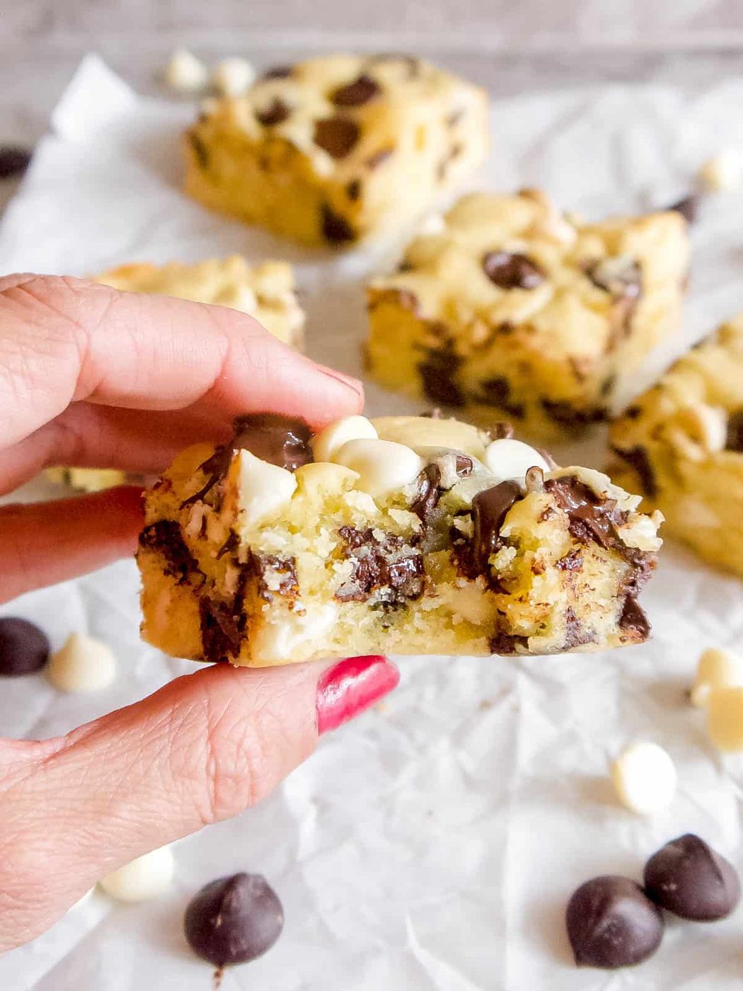 A slice of white chocolate brownies in someone's hands with a bite taken out of it.