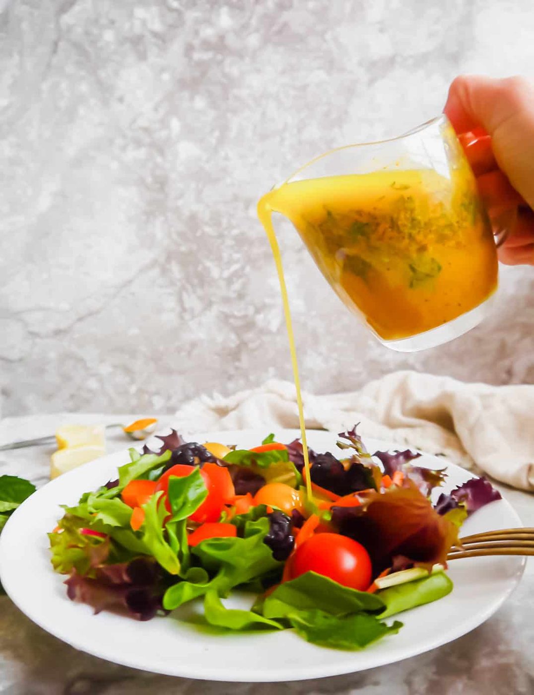Lemon turmeric dressing with mint being poured onto a salad.