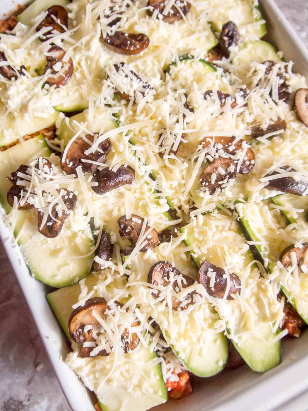 Some shredded cheese added on top of the uncooked lasagna.