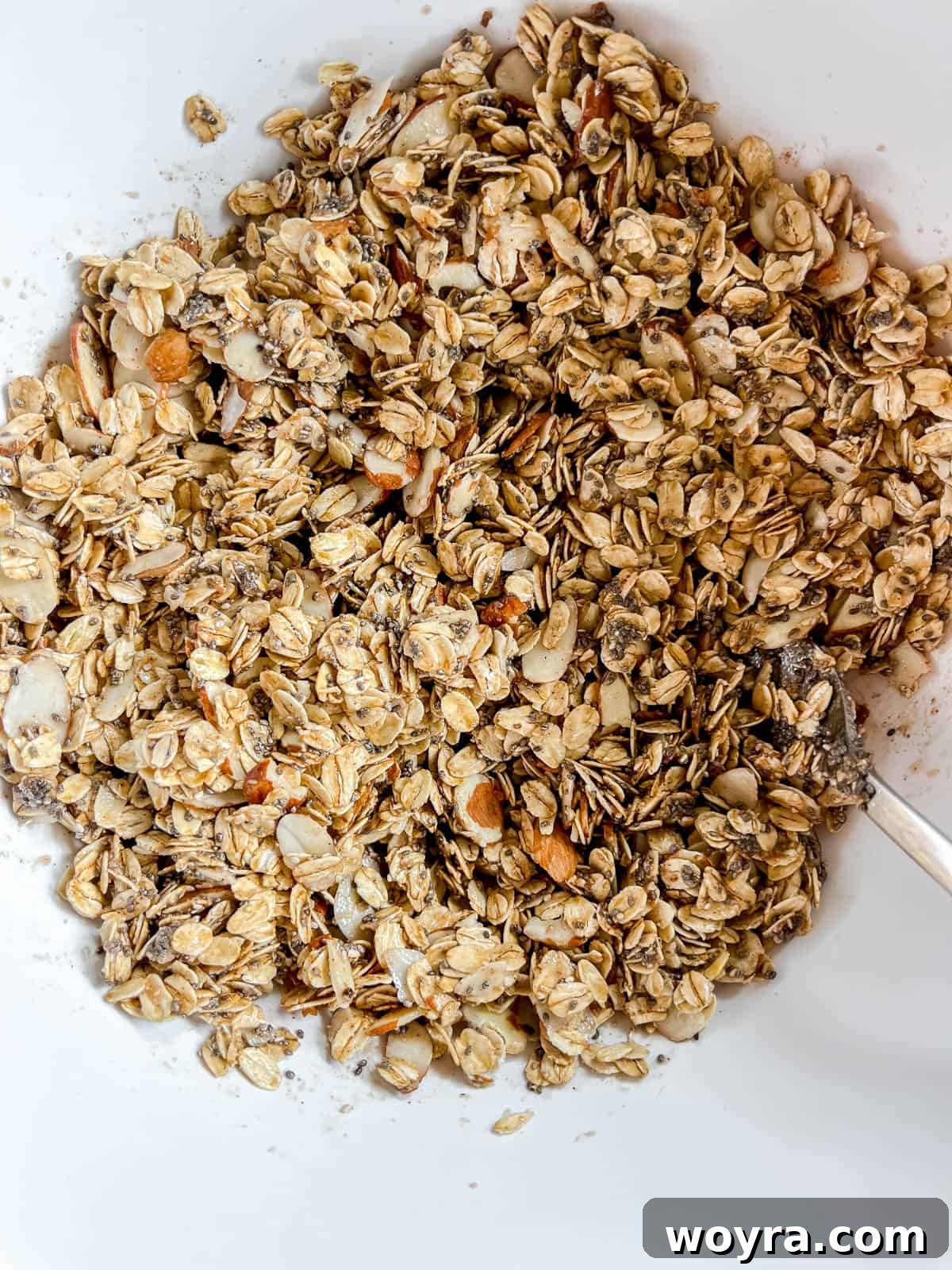 Artisan Olive Oil Granola Almonds and Chia 7 The liquid mixture of maple syrup, olive oil, and vanilla being poured over the mixed dry granola ingredients in a large bowl, ready for coating.