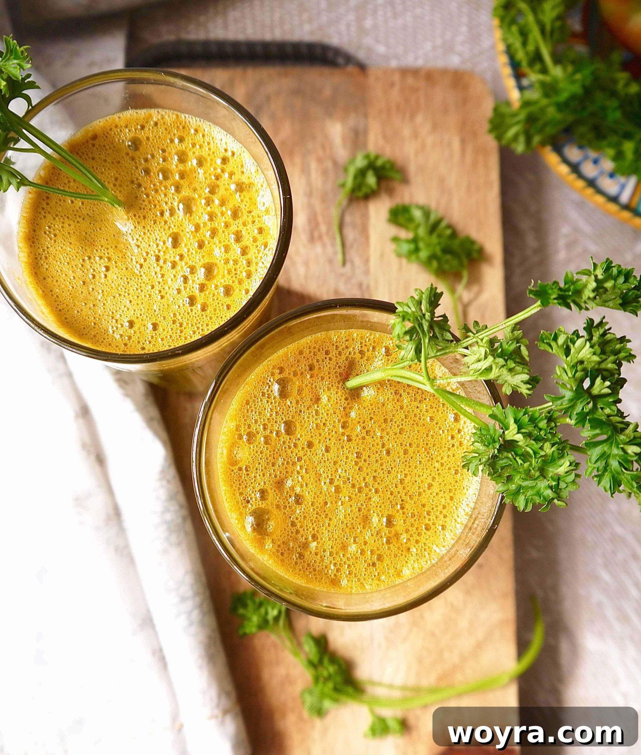 Root to Leaf Radiance 2 Two glasses of vibrant green carrot, kale, apple, and parsley juice, garnished with fresh parsley sprigs, set on a rustic wooden table.
