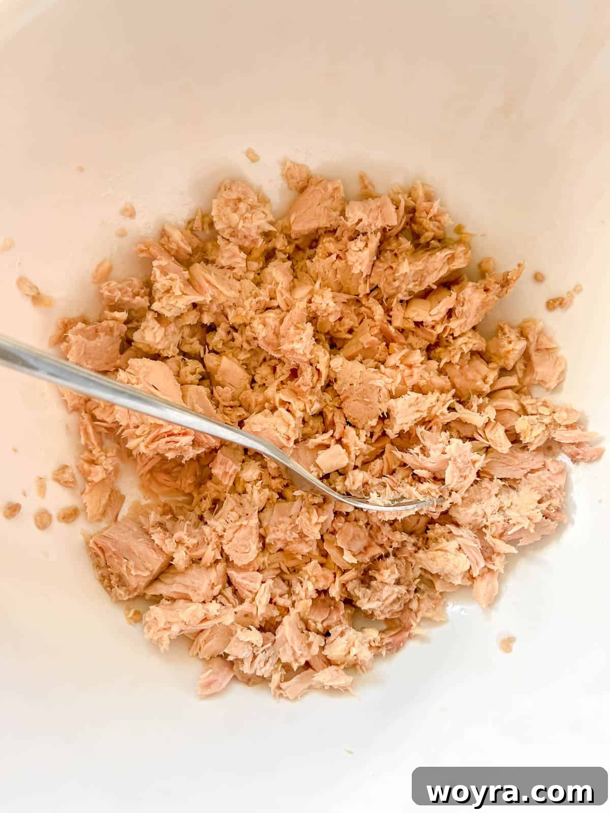 Paleo Whole30 French Tuna Potato Salad 5 Canned tuna in a bowl, being broken into smaller, flaky pieces with a fork.