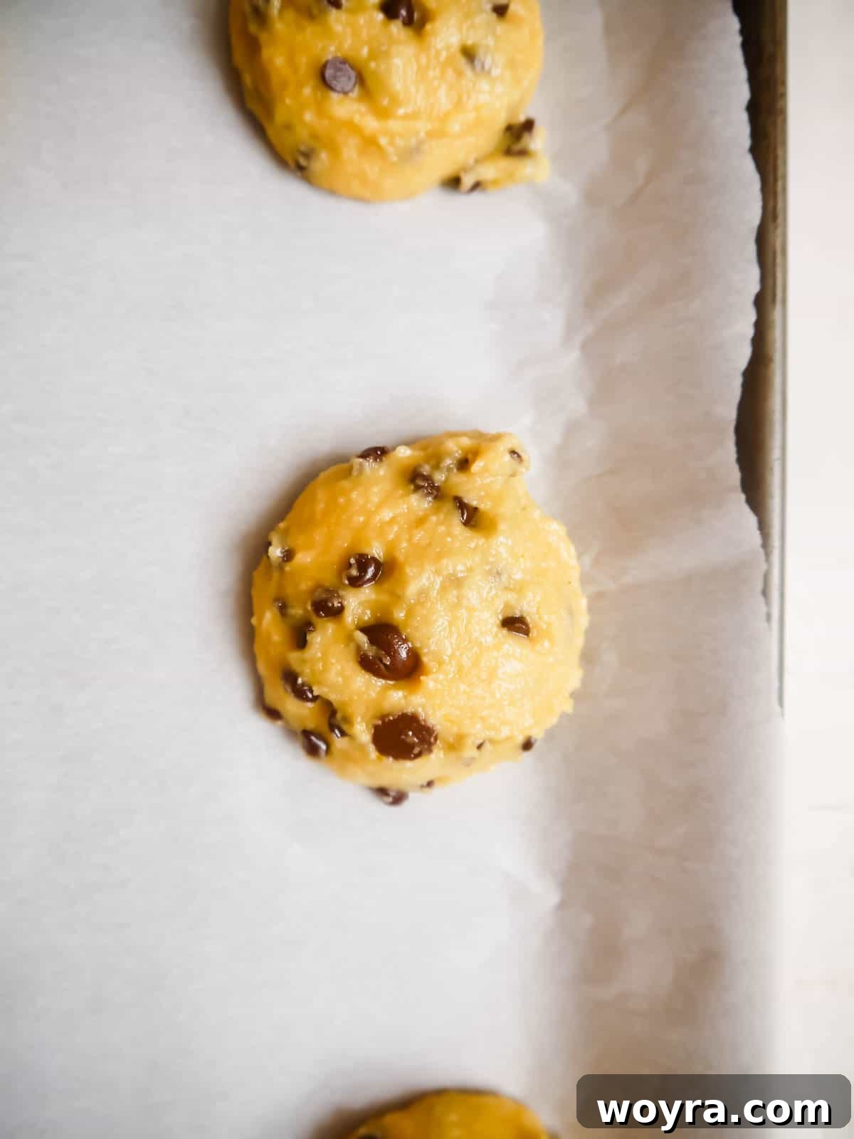 Paleo chocolate chip cookie dough balls neatly arranged on a parchment-lined baking sheet, ready for baking.