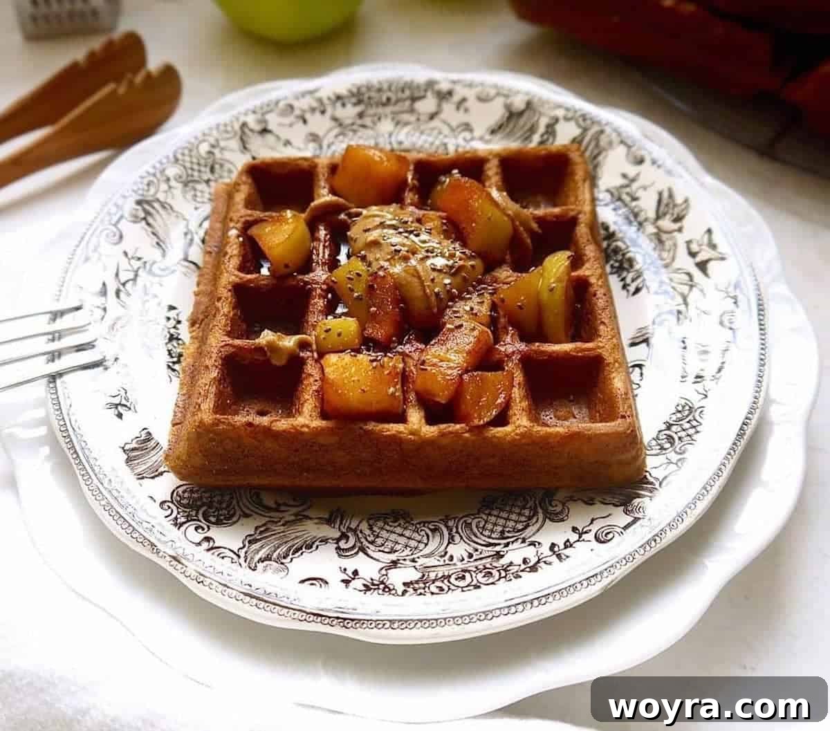 A perfectly cooked stack of paleo apple cinnamon waffles on a plate, adorned with more cooked apples and a generous drizzle of maple syrup.