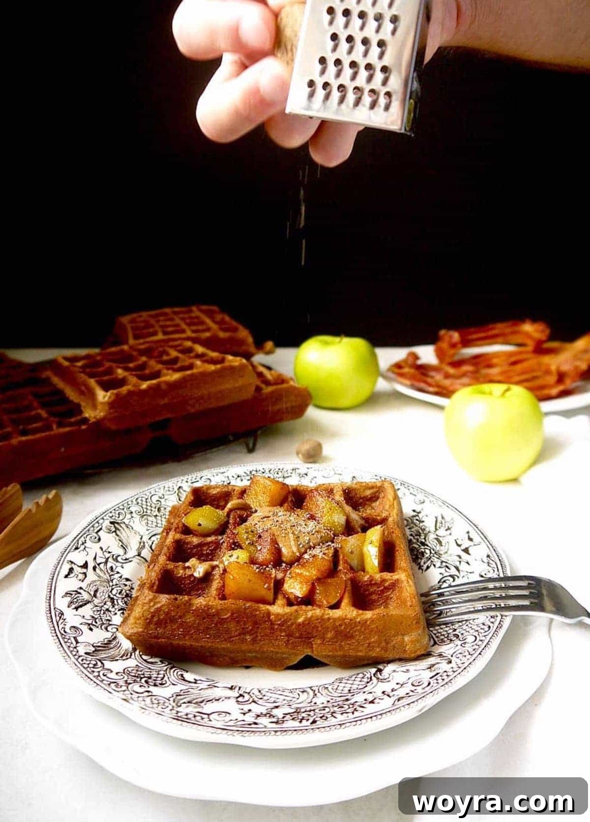 Healthy apple waffles with a light dusting of freshly grated nutmeg being applied on top, highlighting the fragrant spice.