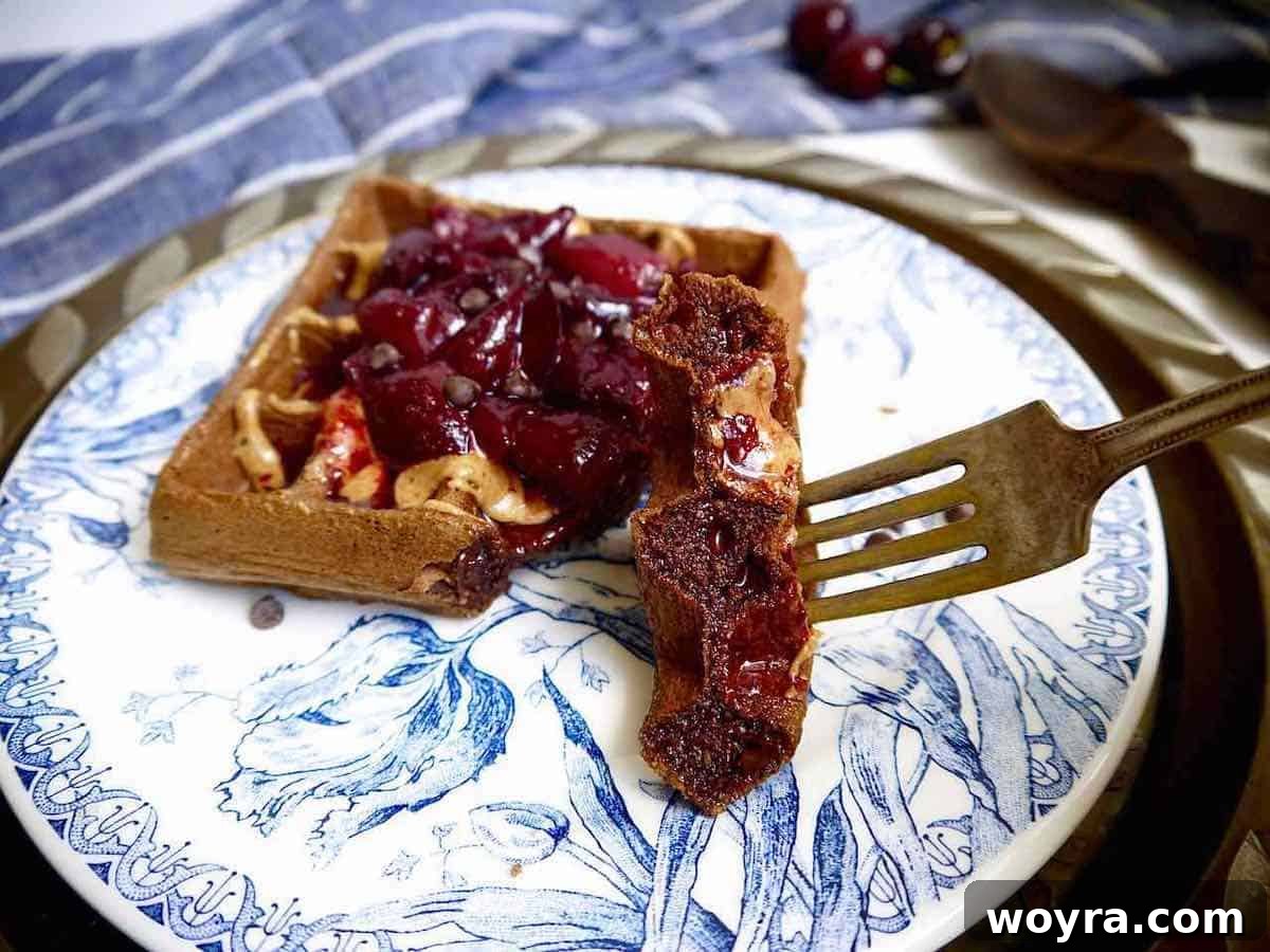 Indulgent Paleo Chocolate Cherry Waffles 7 A close-up of a bite taken from a chocolate cherry waffle on a fork, showing the fluffy interior and melted chocolate.