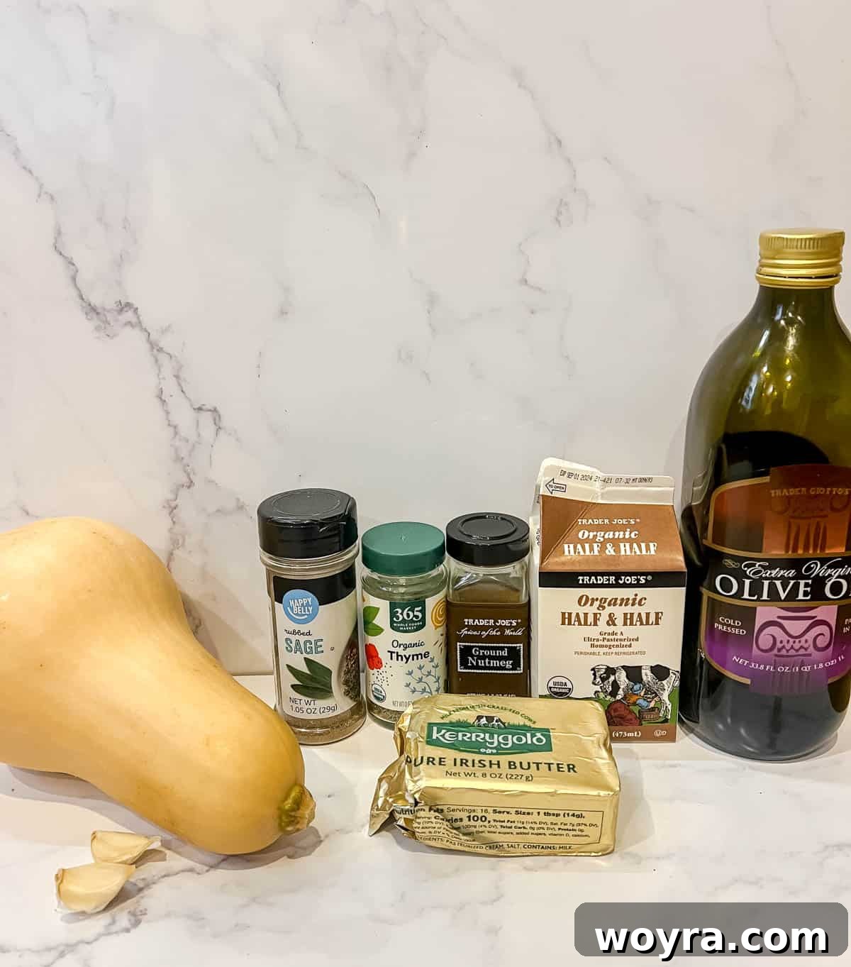A selection of fresh ingredients including a whole butternut squash, garlic, fresh herbs, olive oil, and butter, laid out for mashed butternut squash preparation.