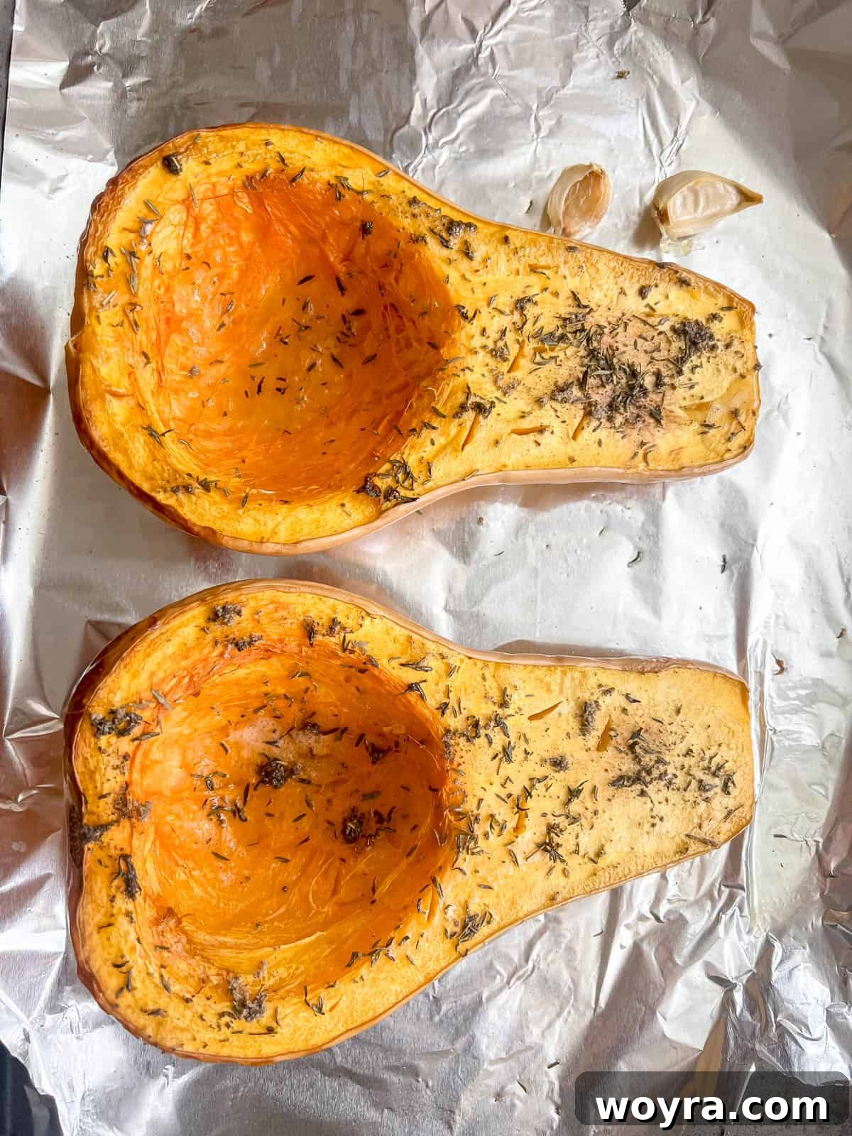 Roasted butternut squash halves in a baking dish with garlic cloves, golden brown and tender.