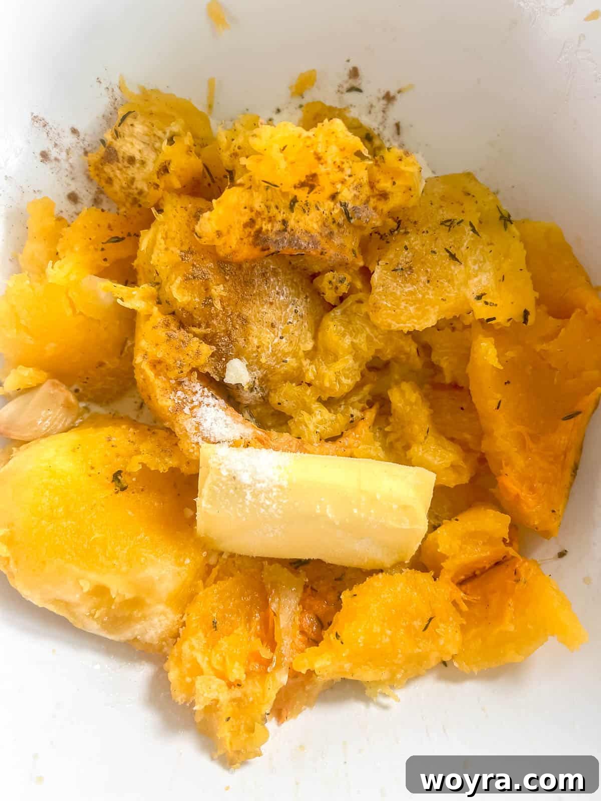 Scooped roasted butternut squash flesh with butter, cream, salt, and pepper in a bowl, before mashing.