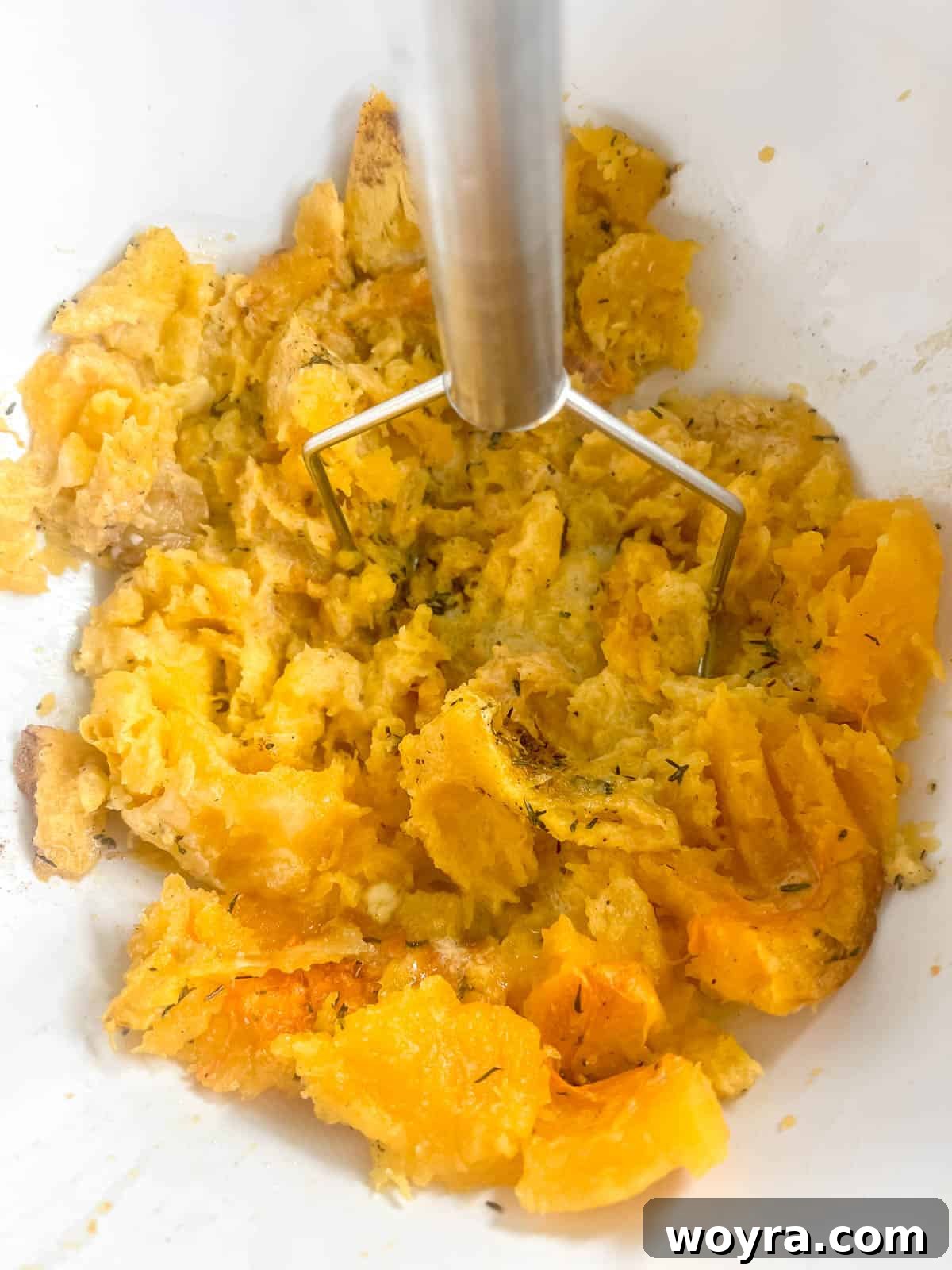 Smooth, creamy mashed butternut squash in a bowl after mashing with a potato masher.