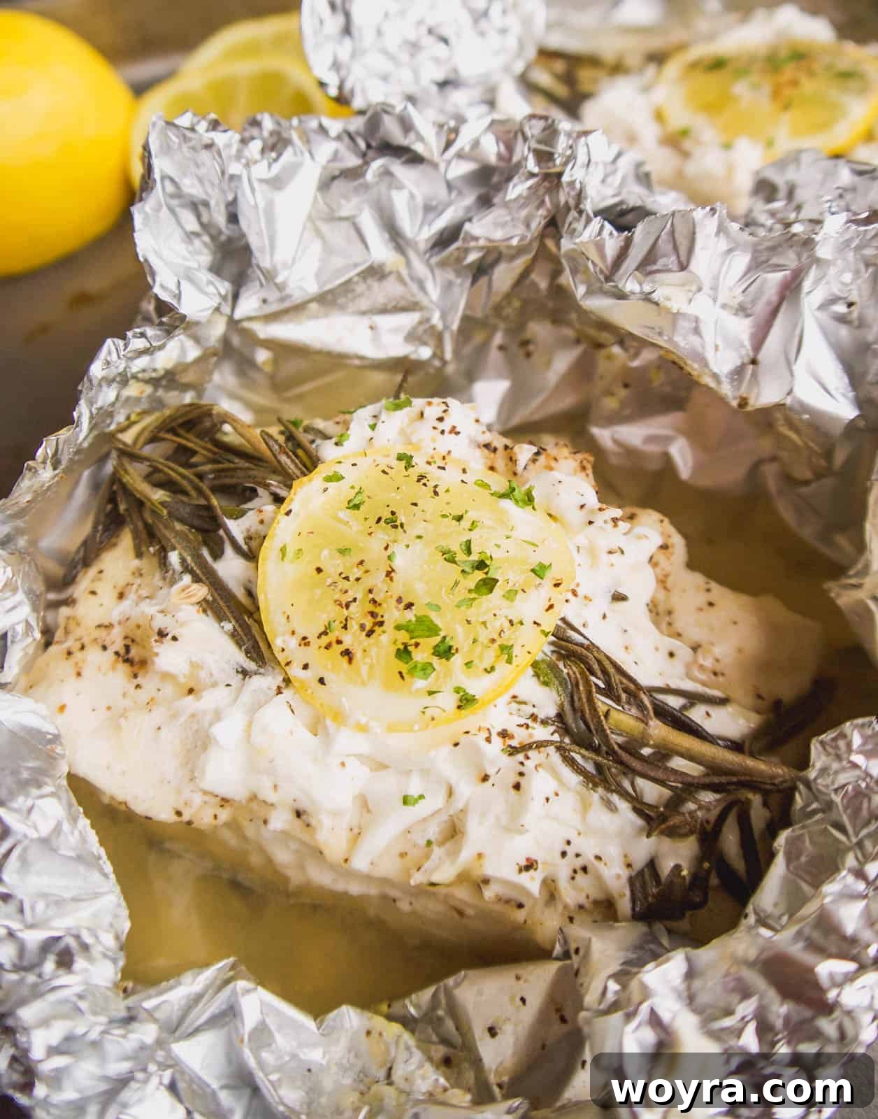 Two foil packets of lemon rosemary halibut, one open revealing the perfectly cooked fish, served alongside fluffy rice.