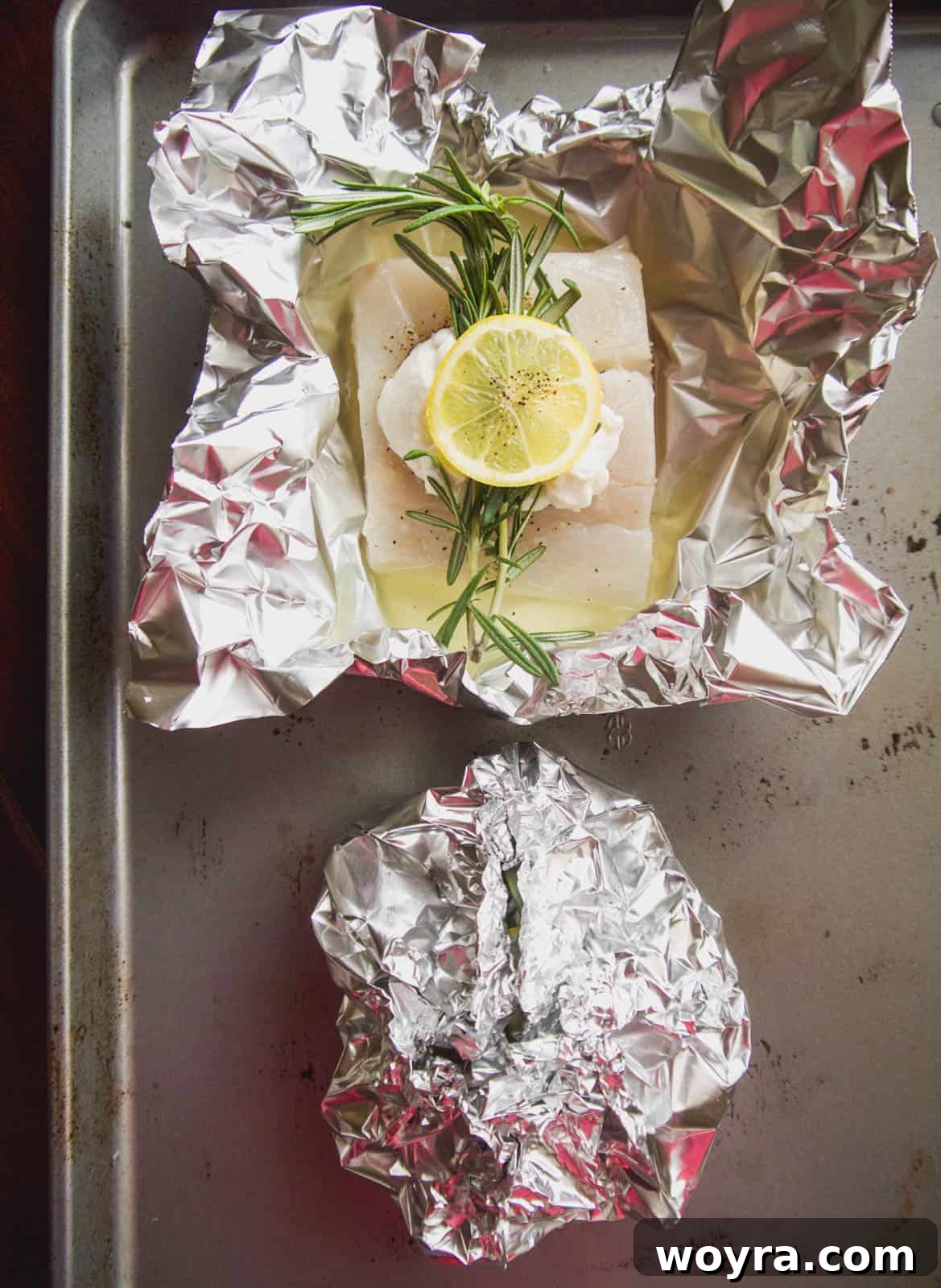 Two tightly sealed fish foil packets on a baking sheet, ready for the oven.