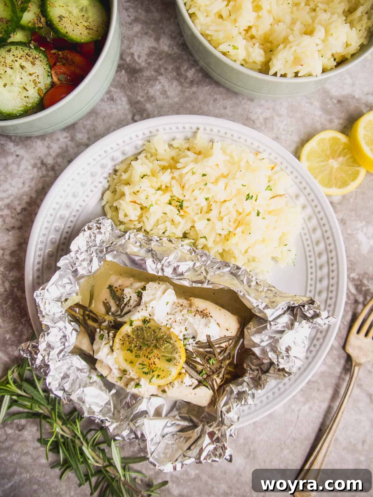 A vibrant close-up of oven-baked halibut in an opened foil packet, garnished with fresh rosemary and lemon slices.