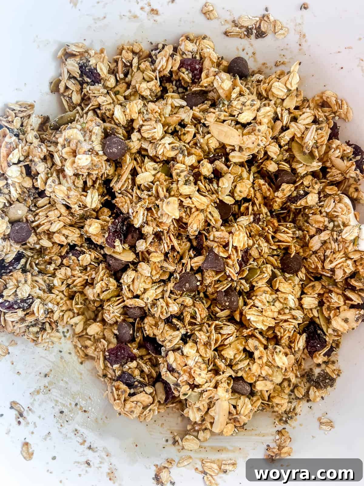 The melted almond butter mixture being poured into the large bowl of dry ingredients, ready to be mixed.