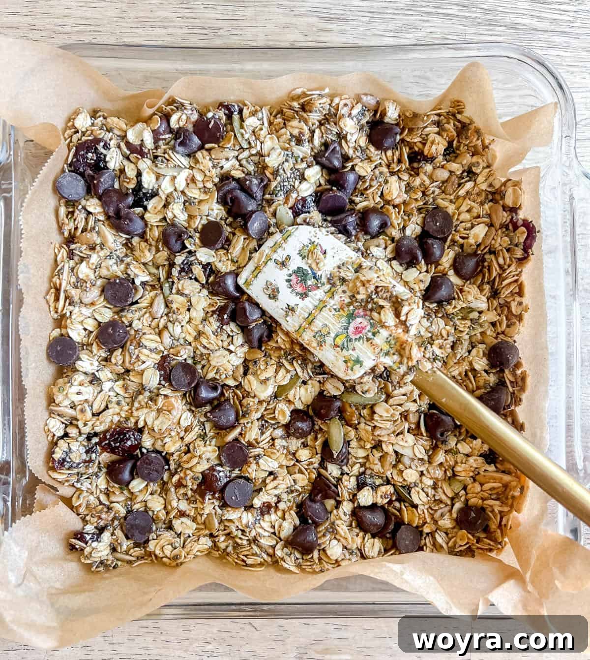 The granola bar mixture pressed firmly into a parchment-lined square pan, with additional chocolate chips on top.