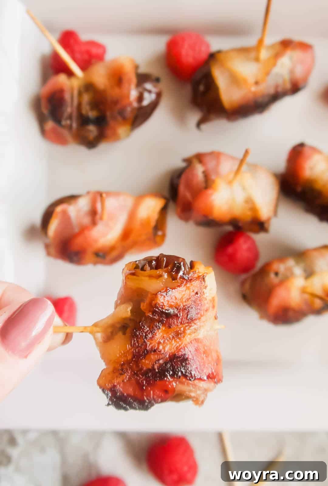 Crispy Bacon-Wrapped Raspberry Stuffed Dates 3 Raspberry stuffed medjool date covered in bacon being lifted by a tooth pick.