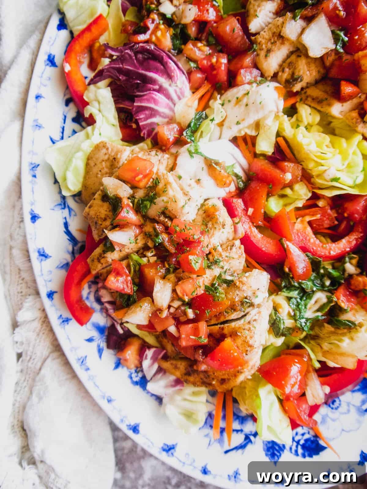 A beautifully arranged grilled chicken bruschetta salad on a white plate, drizzled with balsamic dressing.