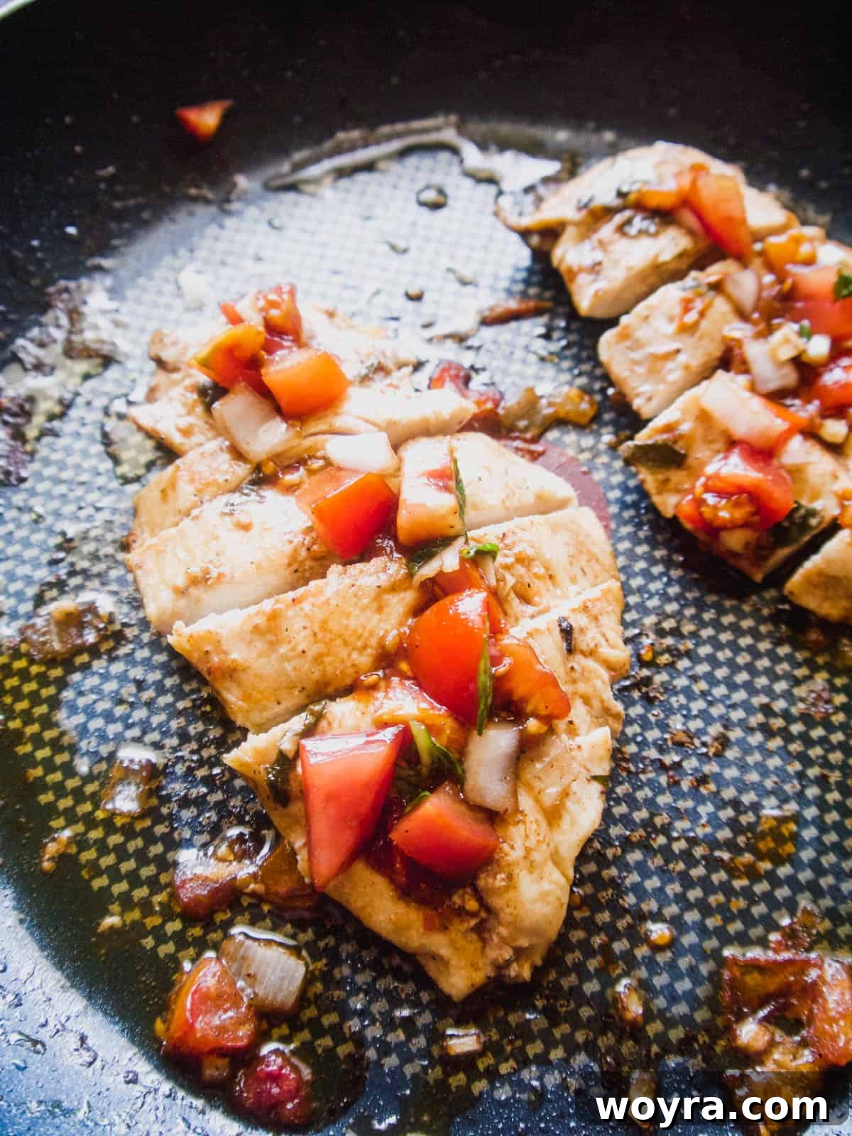 Chicken slices cooking in a frying pan with a portion of bruschetta mixture on top.