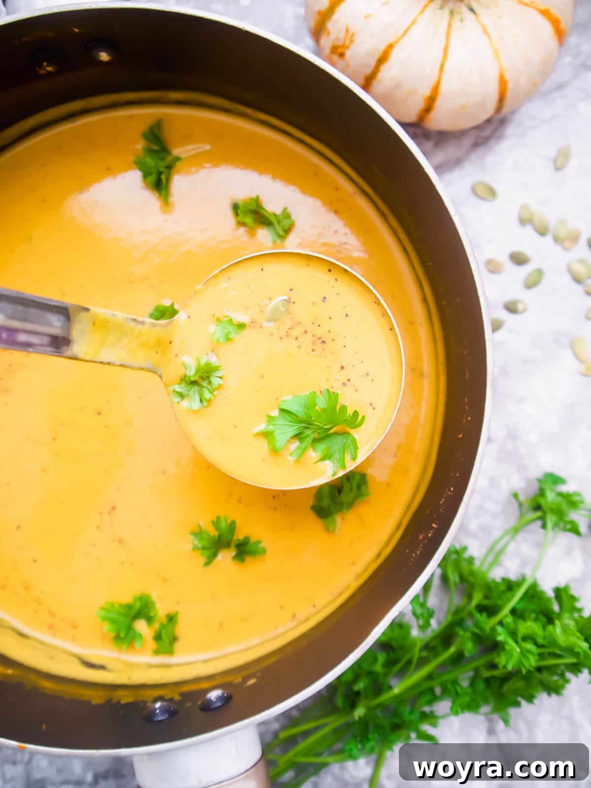 A ladle serving a generous portion of steaming sweet potato pumpkin soup into a ceramic bowl, ready for garnishing.