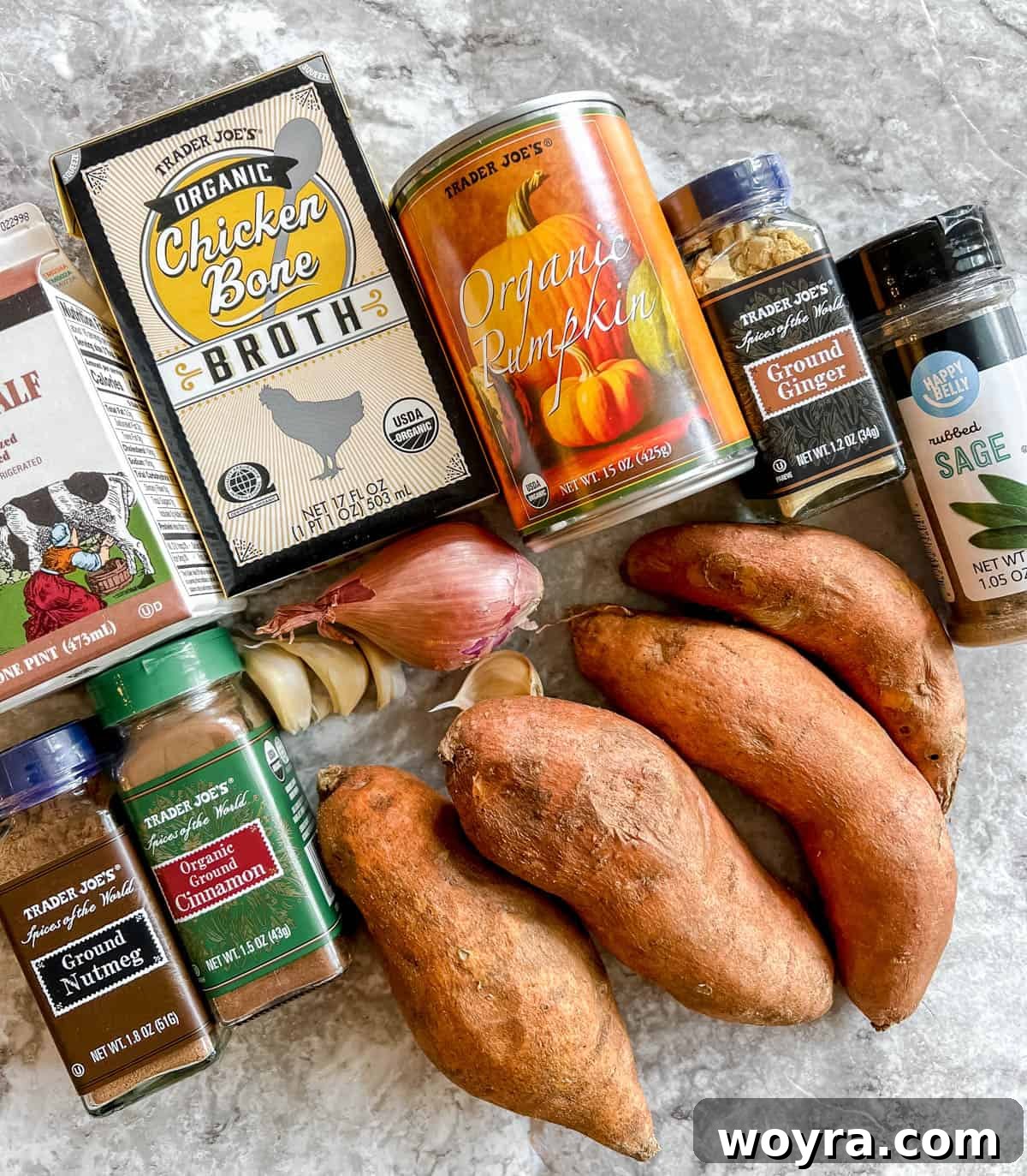 A vibrant selection of fresh ingredients laid out for pumpkin sweet potato soup preparation, including onions, garlic, sweet potatoes, pumpkin puree, and an array of spices.