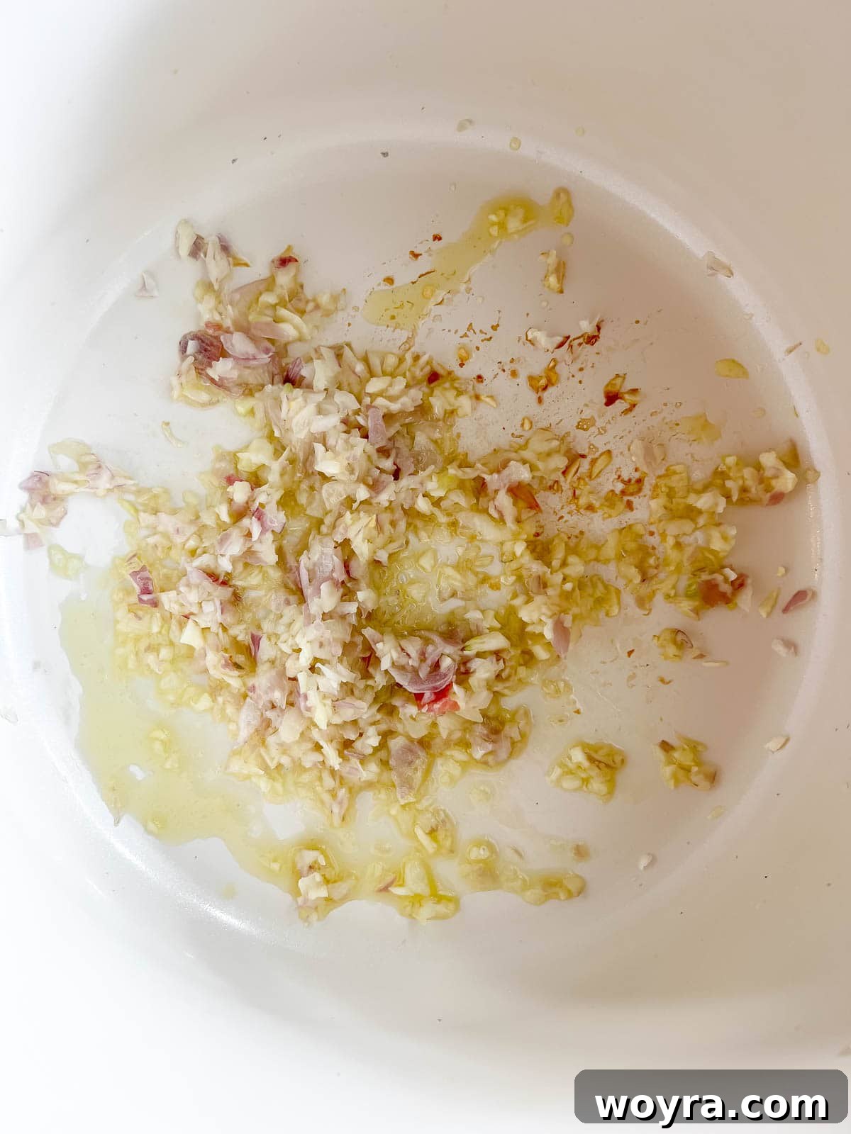 Sliced shallots and minced garlic sizzling in olive oil in a large pan, forming the aromatic base for the soup.