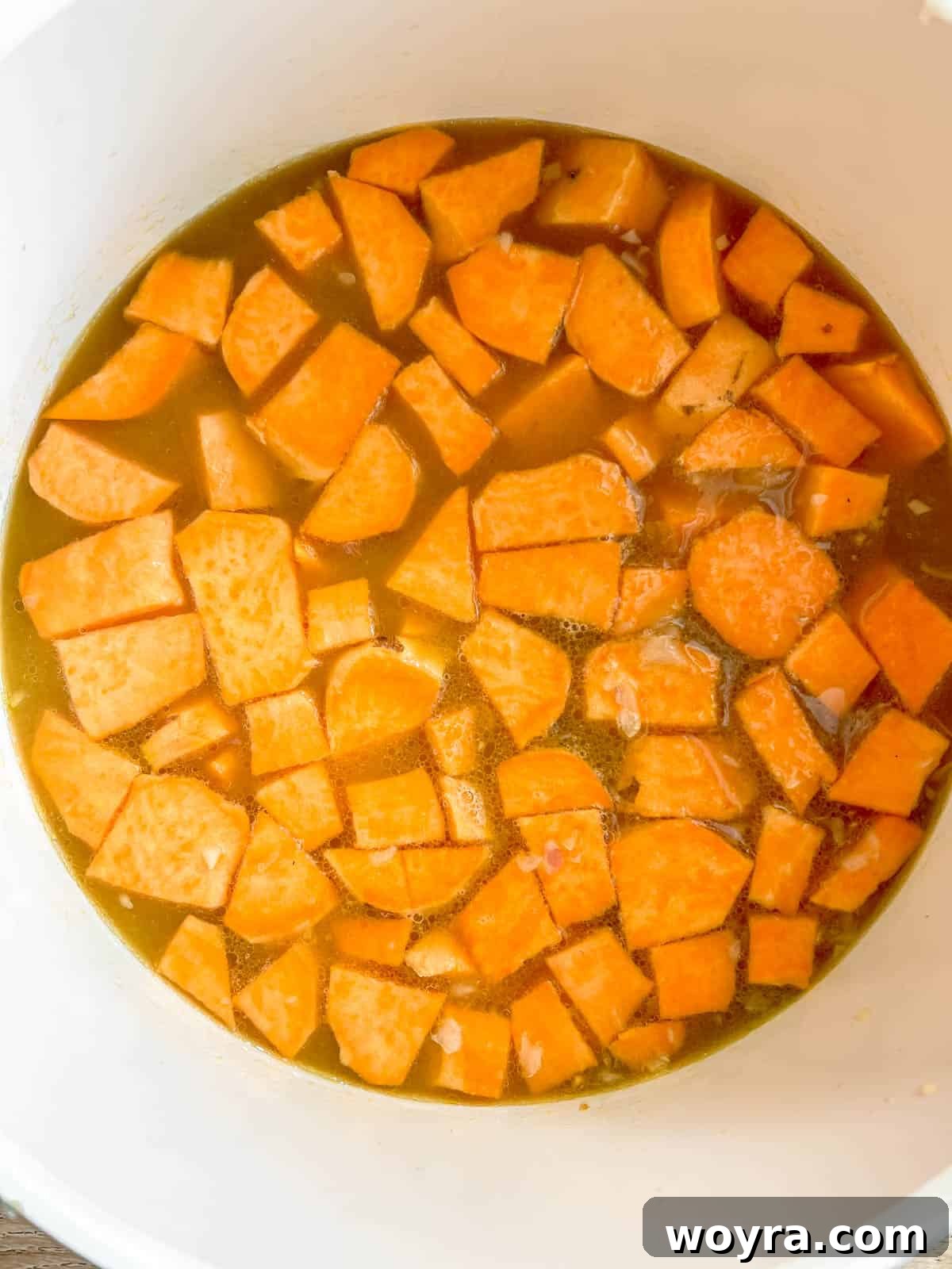 Diced sweet potatoes and bone broth boiling gently in a pan, absorbing flavors and softening.