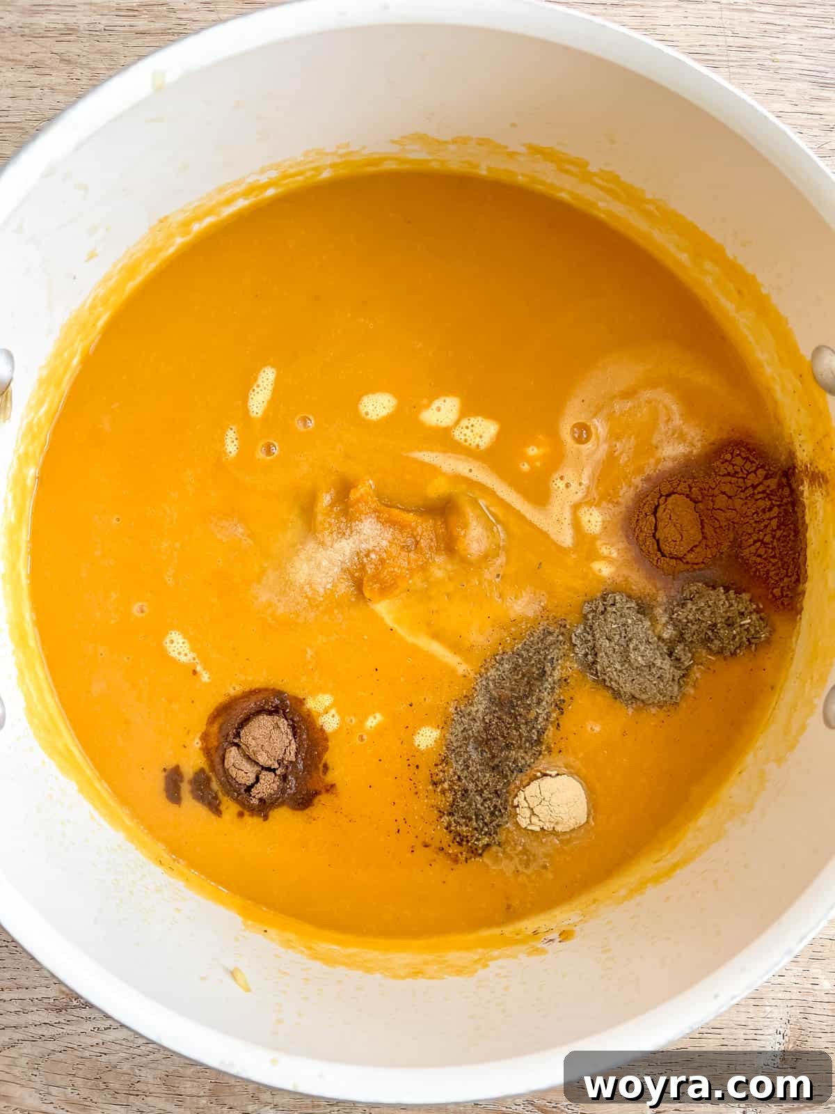 A selection of aromatic spices, including cinnamon, salt, pepper, nutmeg, ginger, sage, and cumin, being added to the pumpkin sweet potato soup for flavoring.