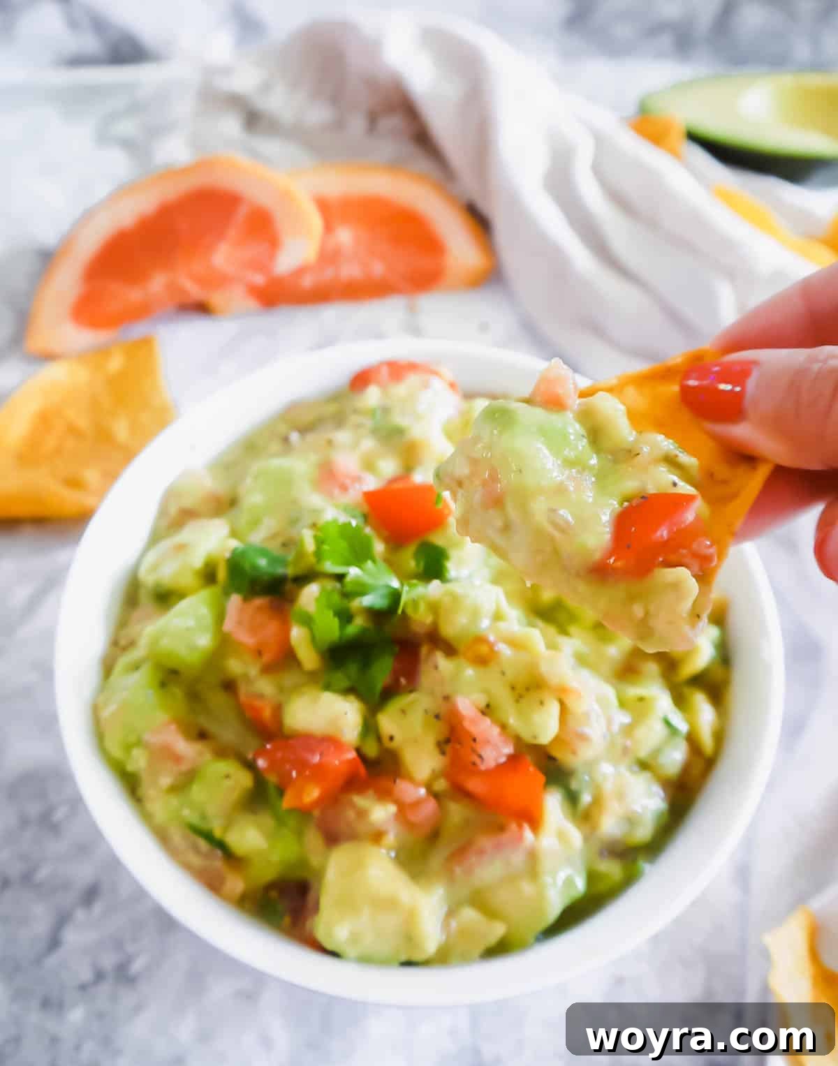 A hand dipping a crispy chip into a bowl of creamy grapefruit guacamole, capturing the moment of enjoyment.