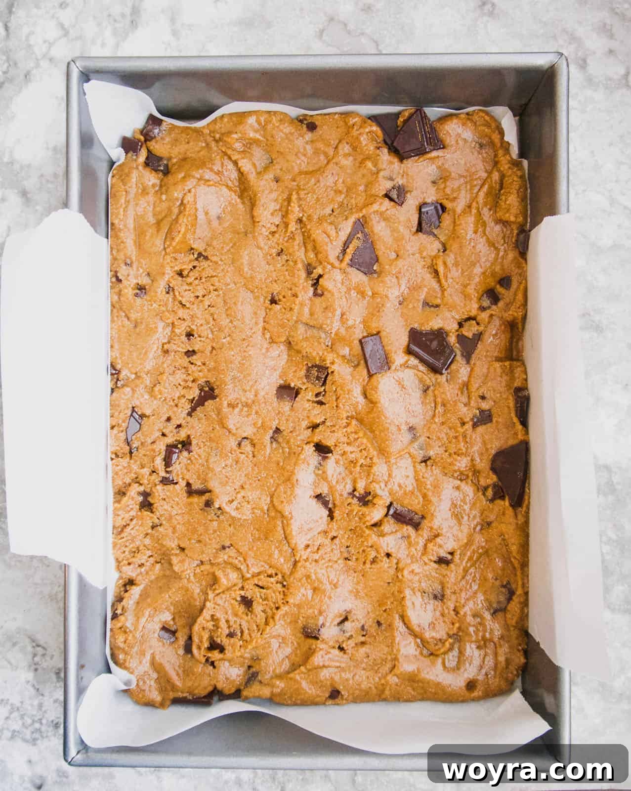 The cookie bar layer pressed evenly into the parchment-lined baking pan.