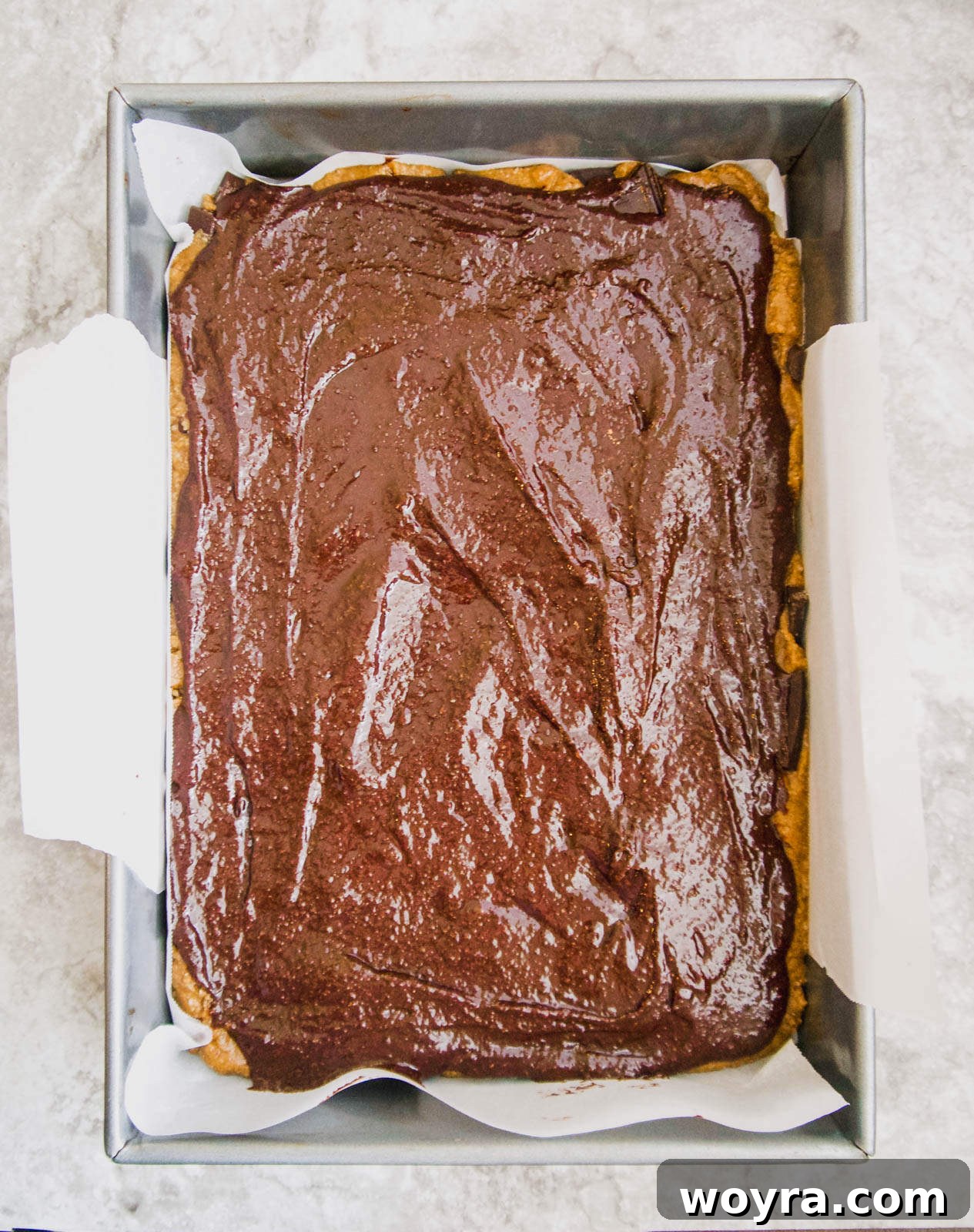 The combined raw brookies, with brownie batter evenly spread over the cookie layer, ready for baking.