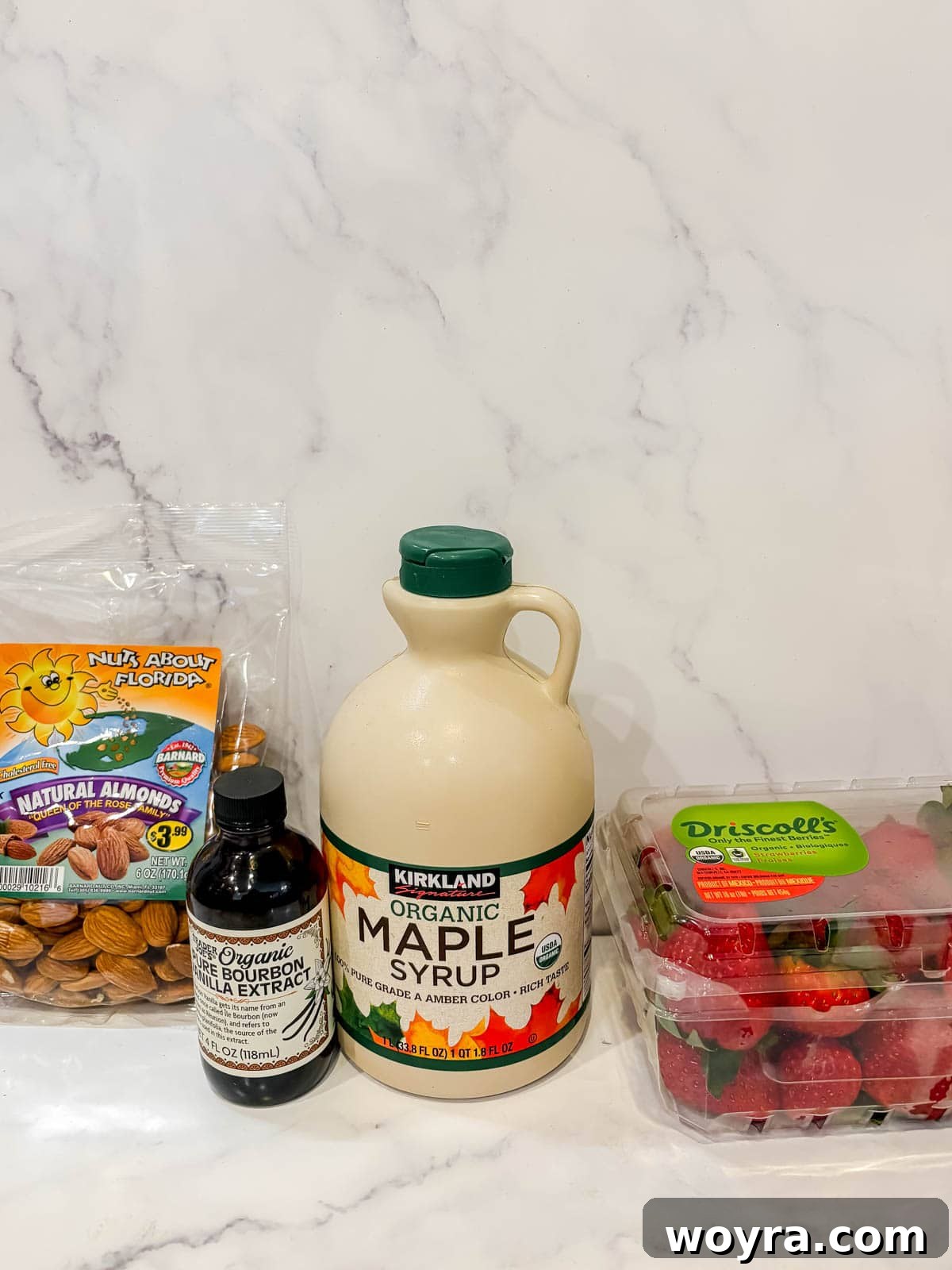 Homemade Strawberry Almond Milk: A Vegan Delight 2 A flat lay photograph showcasing the key ingredients for homemade strawberry almond milk: raw almonds, sliced fresh strawberries, a bottle of maple syrup, and vanilla extract.