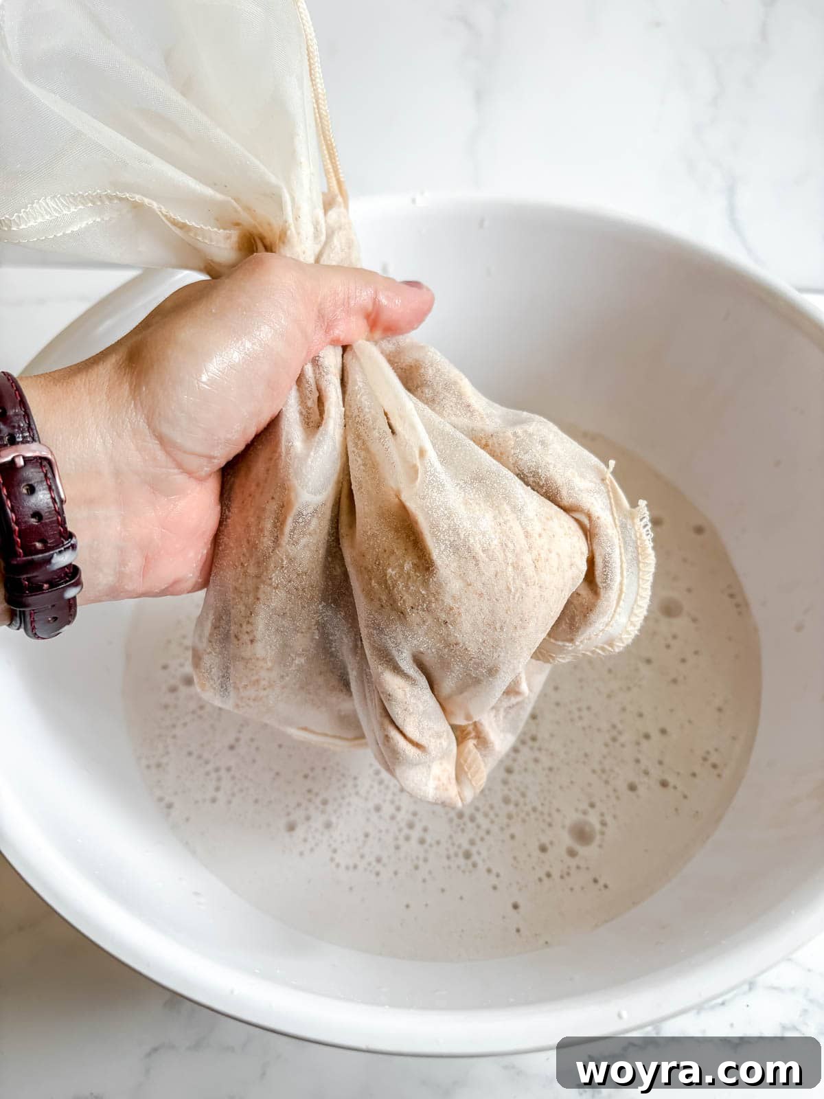 Homemade Strawberry Almond Milk: A Vegan Delight 11 A hand firmly squeezing a nut milk bag to extract the last drops of creamy almond milk into a bowl.