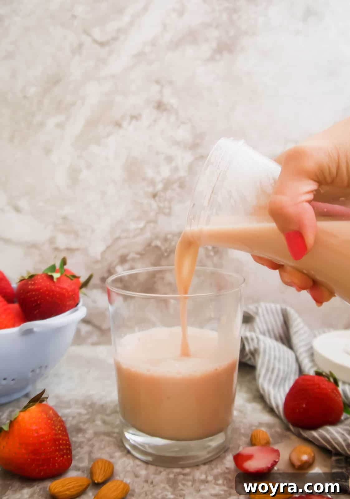 Homemade Strawberry Almond Milk: A Vegan Delight 14 A glass of homemade strawberry almond milk being poured into a cup, showing its vibrant pink color and smooth texture.