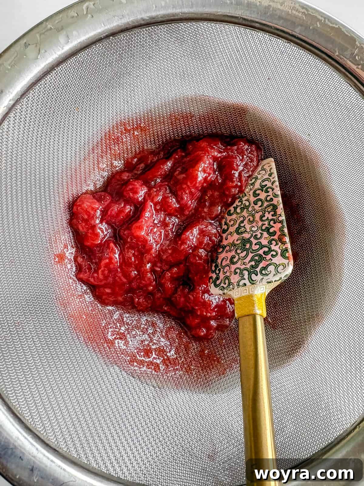 Homemade Strawberry Almond Milk: A Vegan Delight 6 Strawberry pulp being separated from the syrup using a fine mesh strainer, with the liquid syrup collecting in a bowl below.