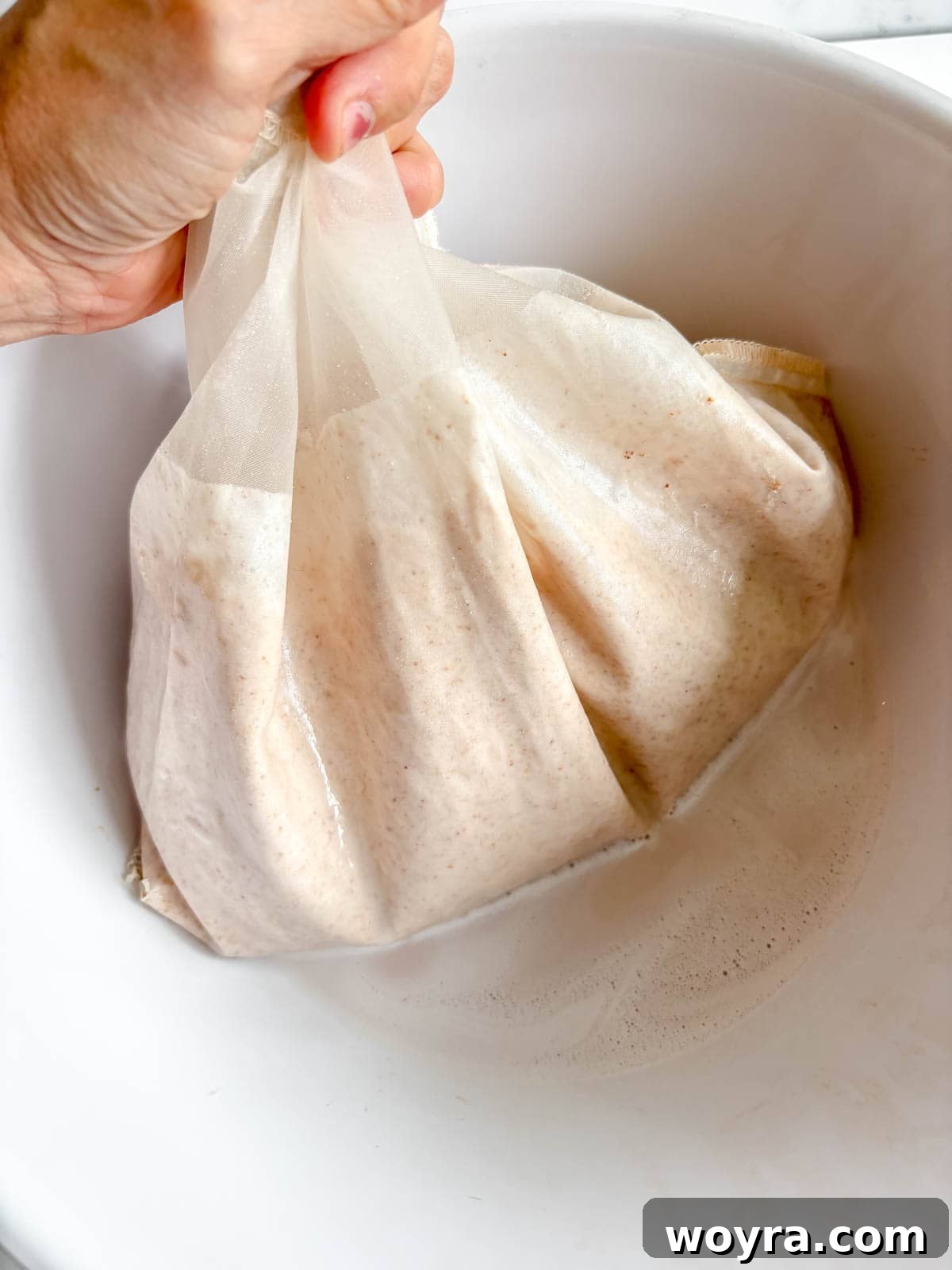 Homemade Strawberry Almond Milk: A Vegan Delight 10 The blended almond milk mixture being poured into a nut milk bag, which is positioned over a large bowl to collect the strained milk.