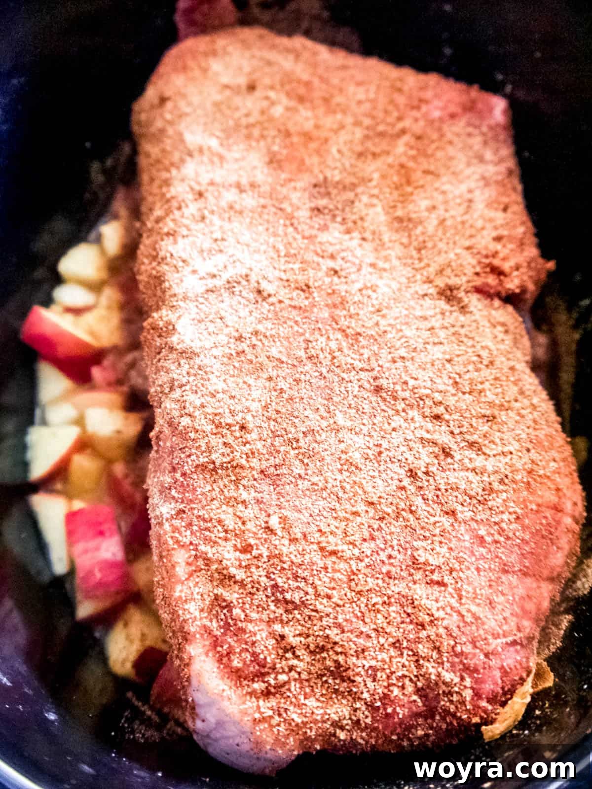 Tender Apple-Infused Pulled Pork 5 Pork shoulder roast seasoned with spices, resting on a bed of diced apples, mustard, honey, and apple juice in the slow cooker before cooking.