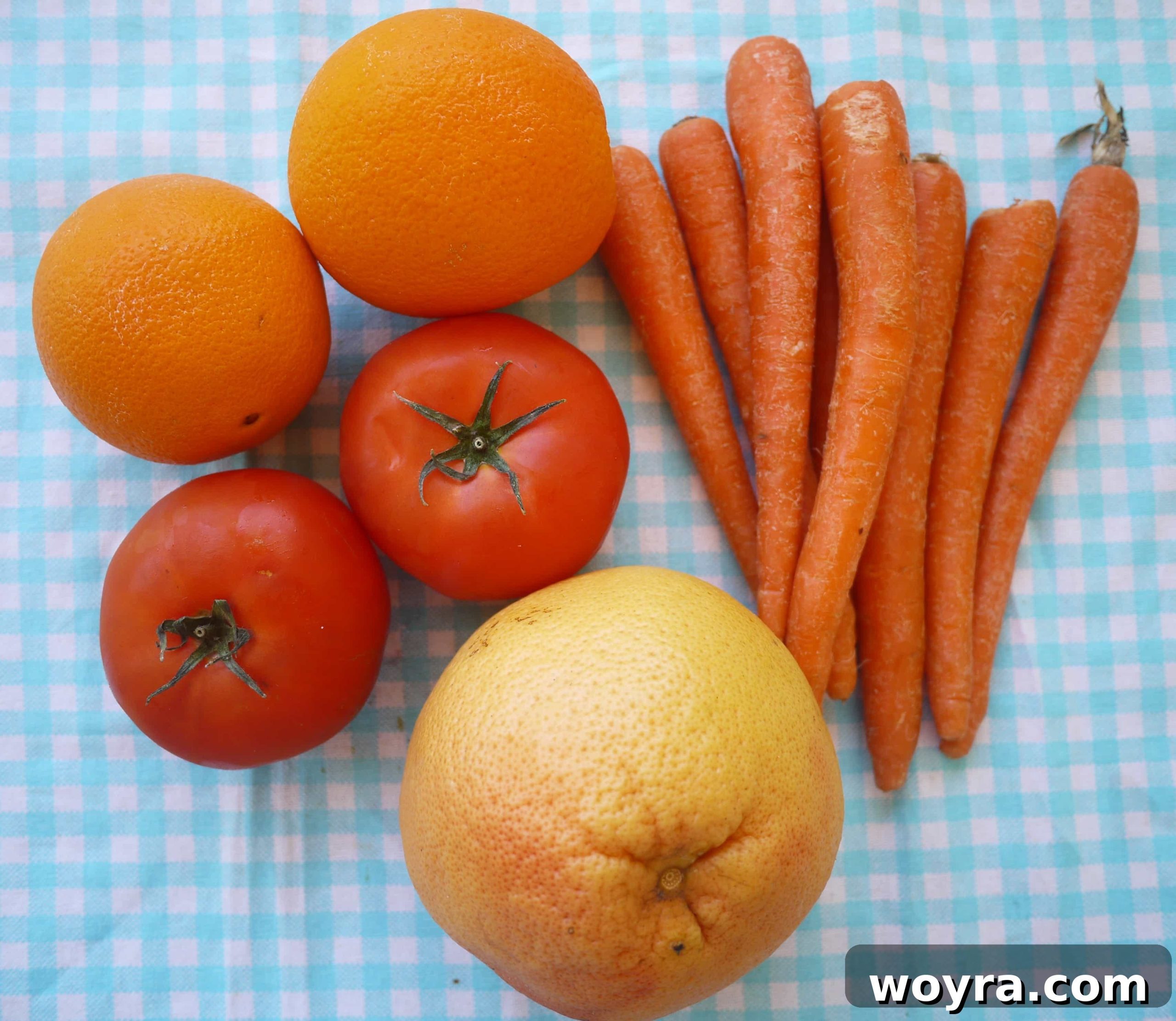 Rejuvenating Tomato Carrot Fusion 3 Fresh organic carrots, ripe red tomatoes, bright oranges, and a juicy grapefruit laid out on a wooden surface, ready for juicing.