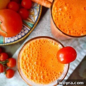 Close-up of a glass of refreshing tomato carrot juice, garnished with fresh ingredients.