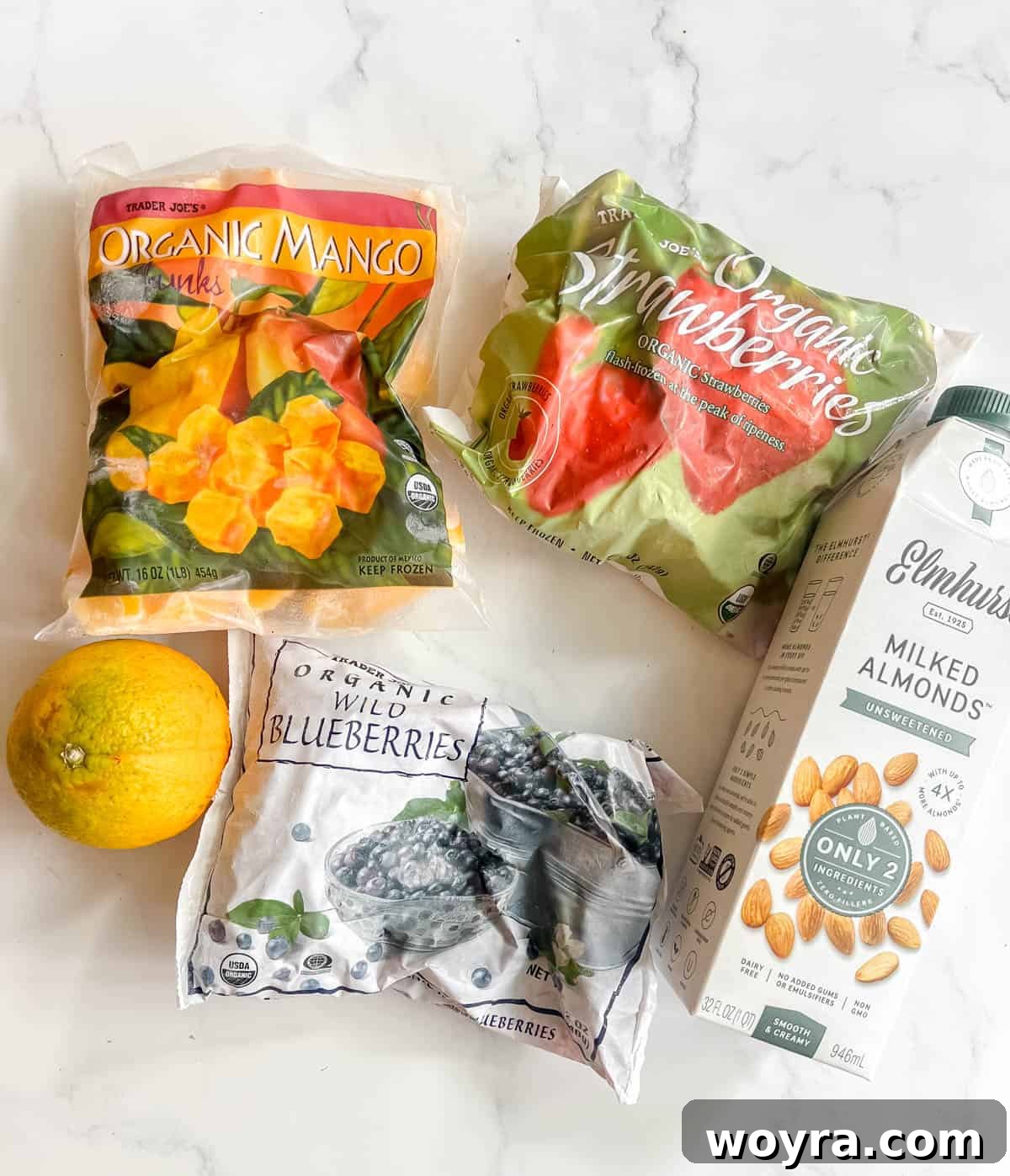 Tropical Pitaya Mango Berry Blend 3 Assortment of fresh and frozen ingredients needed to make dragon fruit powder smoothie, including mango, blueberries, strawberries, orange, and almond milk.