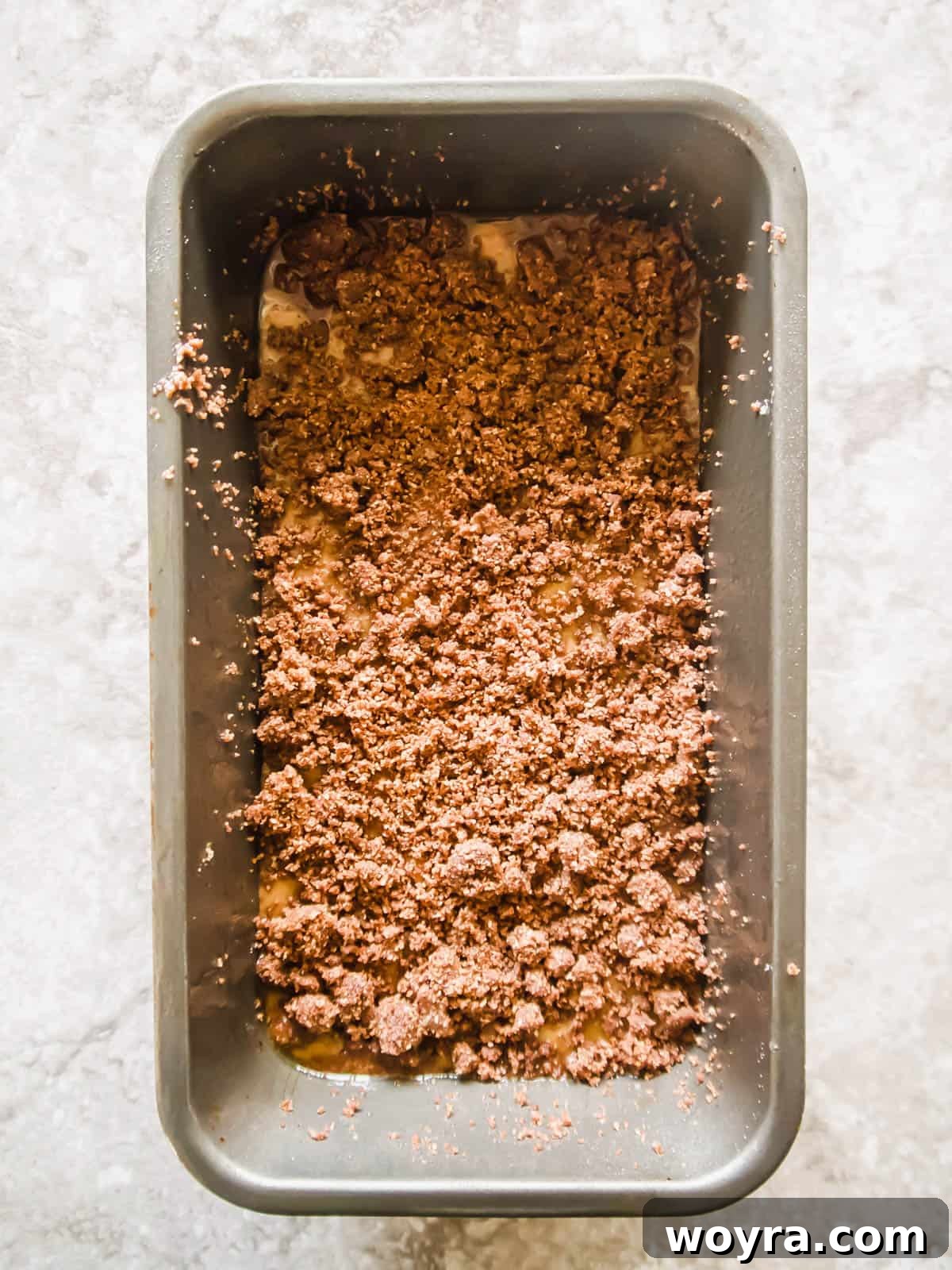 Banana bread coffee cake batter in a loaf tin with the first layer of streusel on top.
