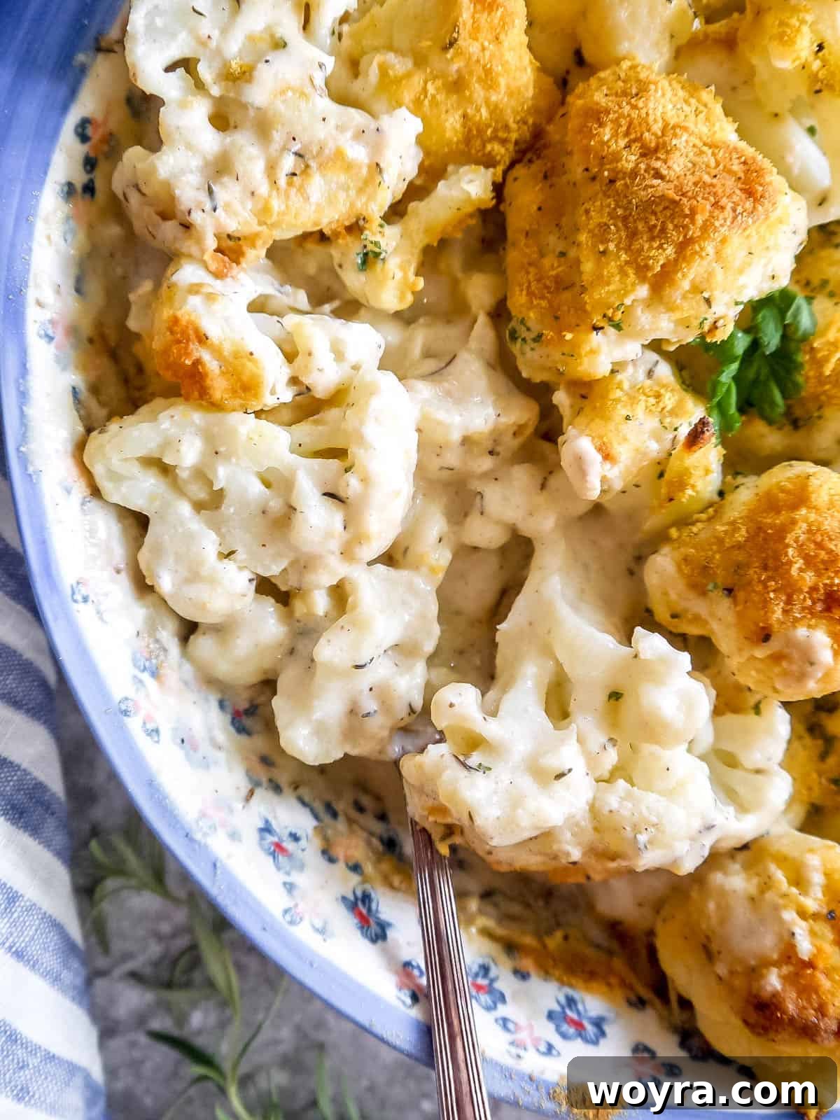 A golden-baked Vegan cauliflower casserole in a ceramic dish, with a serving spoon resting inside, showcasing its creamy texture.