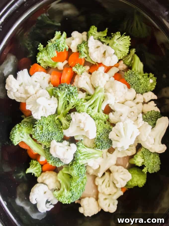 Assorted chopped vegetables, including carrots, potatoes, and cauliflower, added to the slow cooker over the chicken.