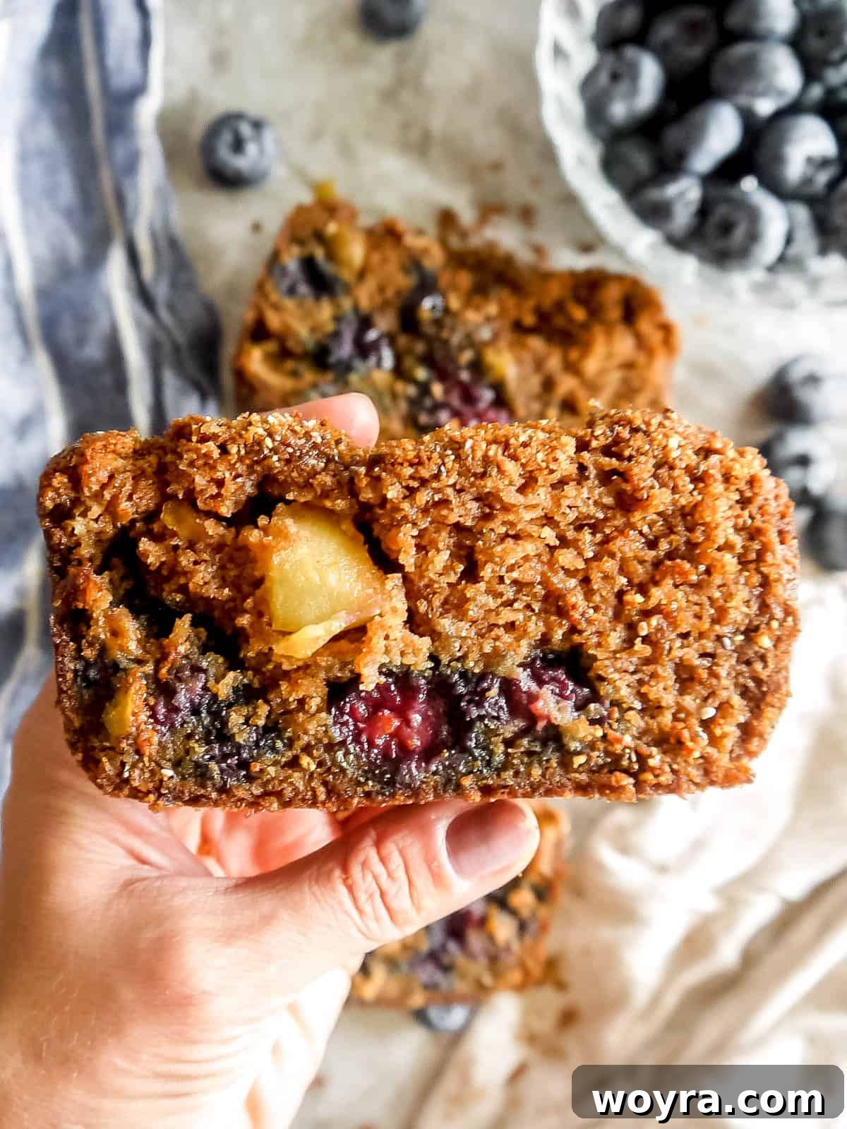 Guilt-Free Paleo Gluten-Free Apple Blueberry Loaf 2 A hand holding a slice of healthy Apple Blueberry Bread, showcasing its crumb topping and fruit chunks.