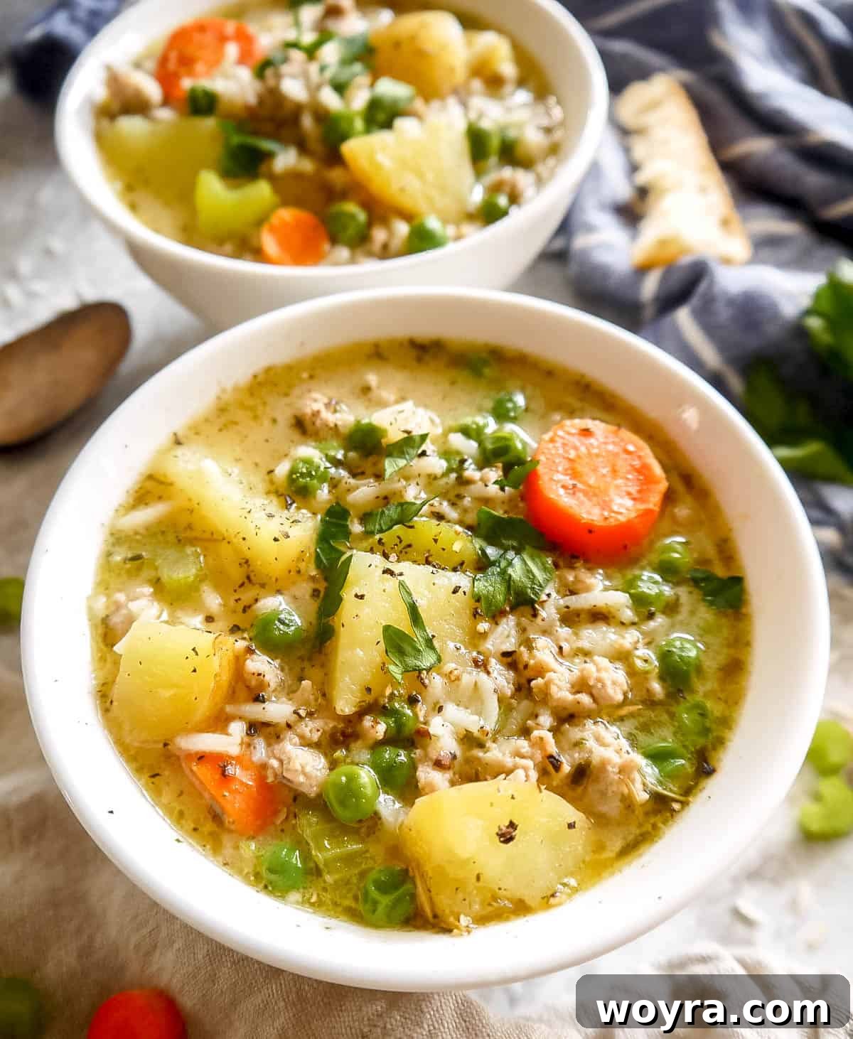 Up close photo of turkey soup with tender potatoes and carrots visible, garnished with fresh greens.