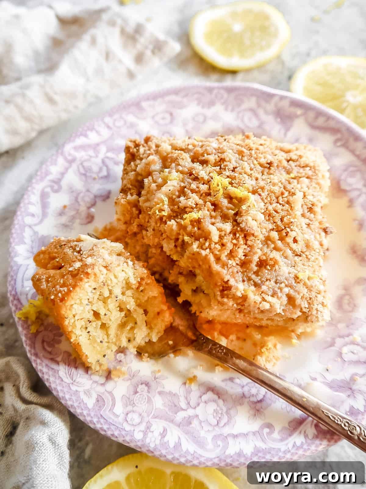 A fork taking a bite out of a moist slice of dairy-free Lemon Poppy Seed Coffee Cake, showcasing its crumbly topping and tender interior.
