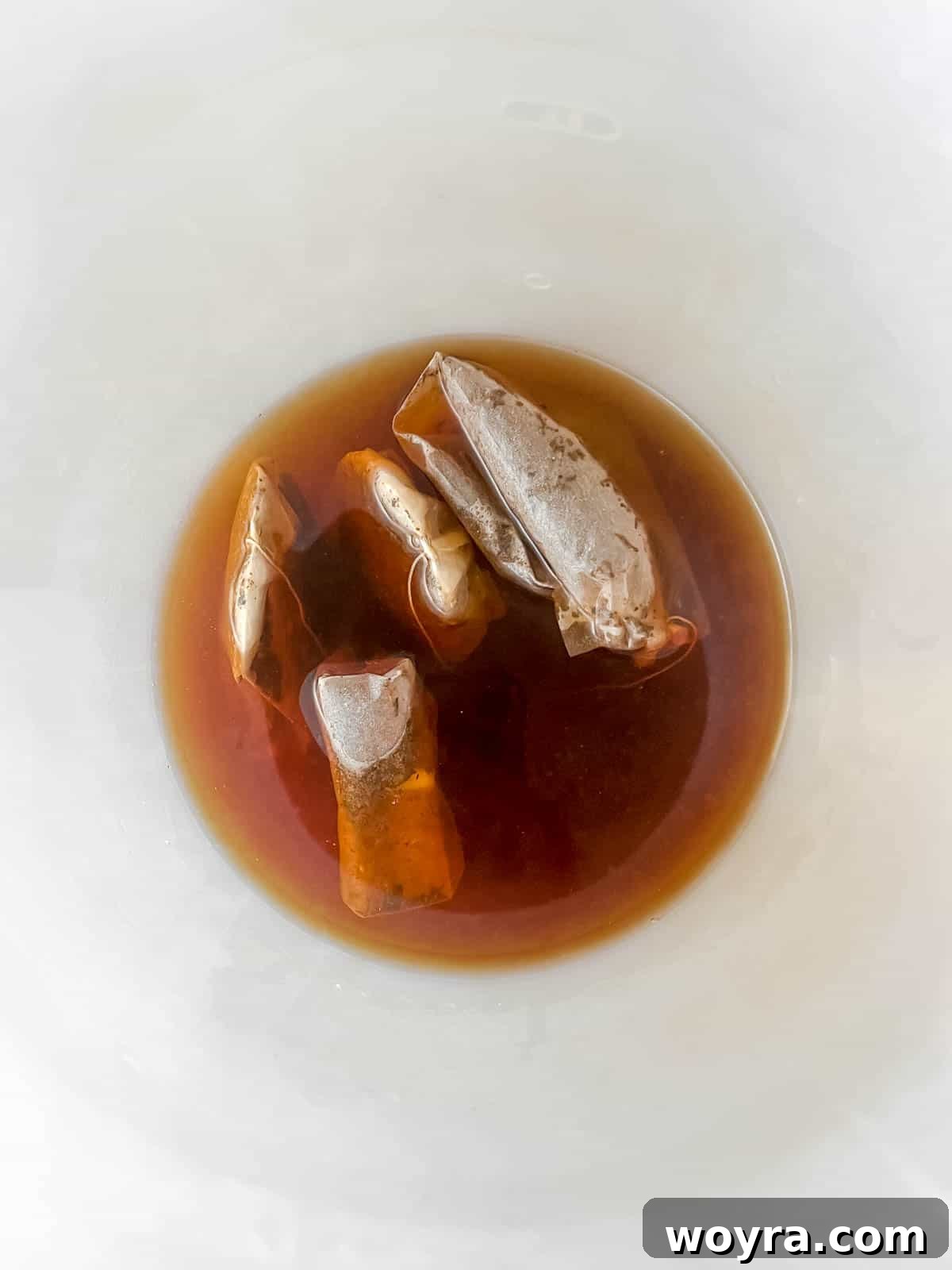Black tea bags steeping in hot water within a large glass pitcher.