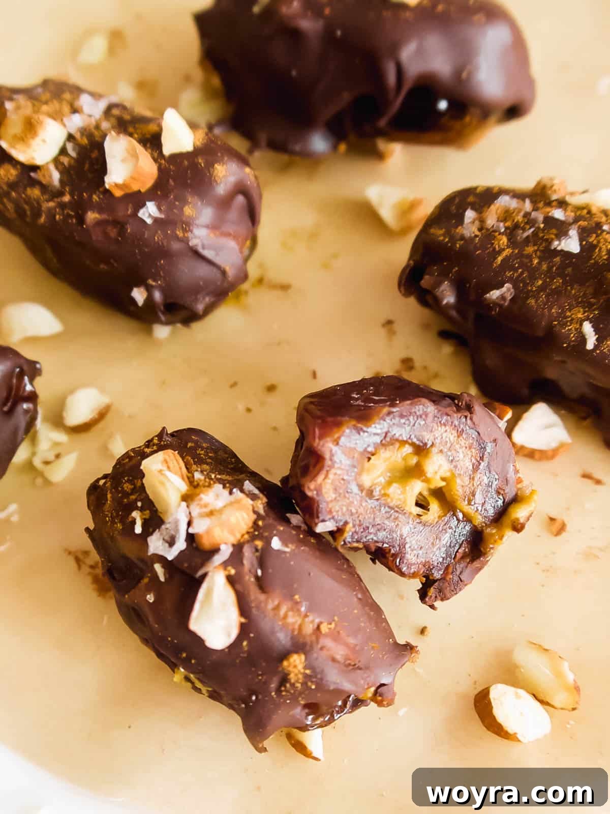 Pumpkin Spice & Chocolate Date Bites 11 Pumpkin dates, one cut in half to show the filling, gracefully surrounded by a scattering of crushed almonds, highlighting their texture and flavor.